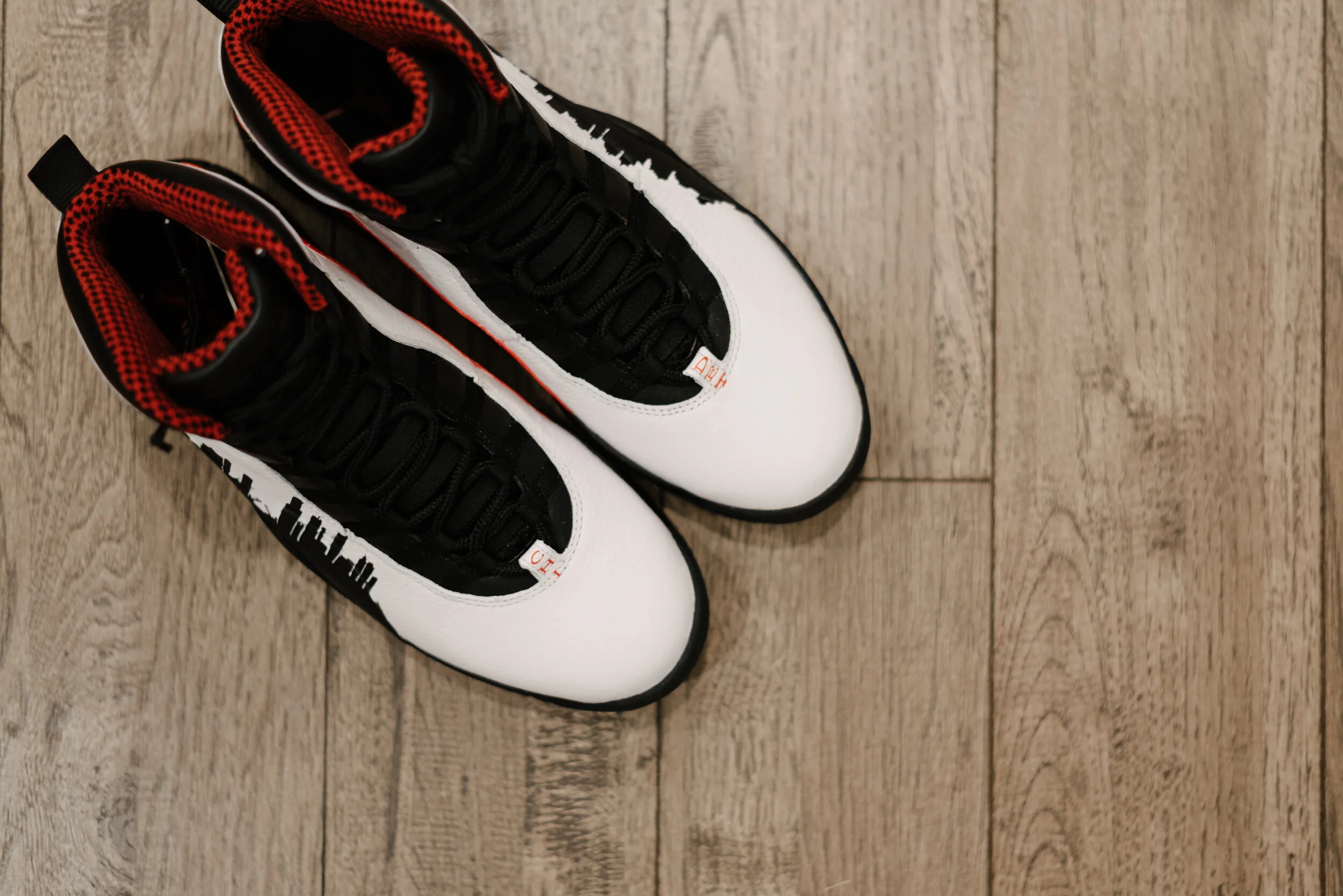 Pair of black, white, and red high-top sneakers on a wooden floor.