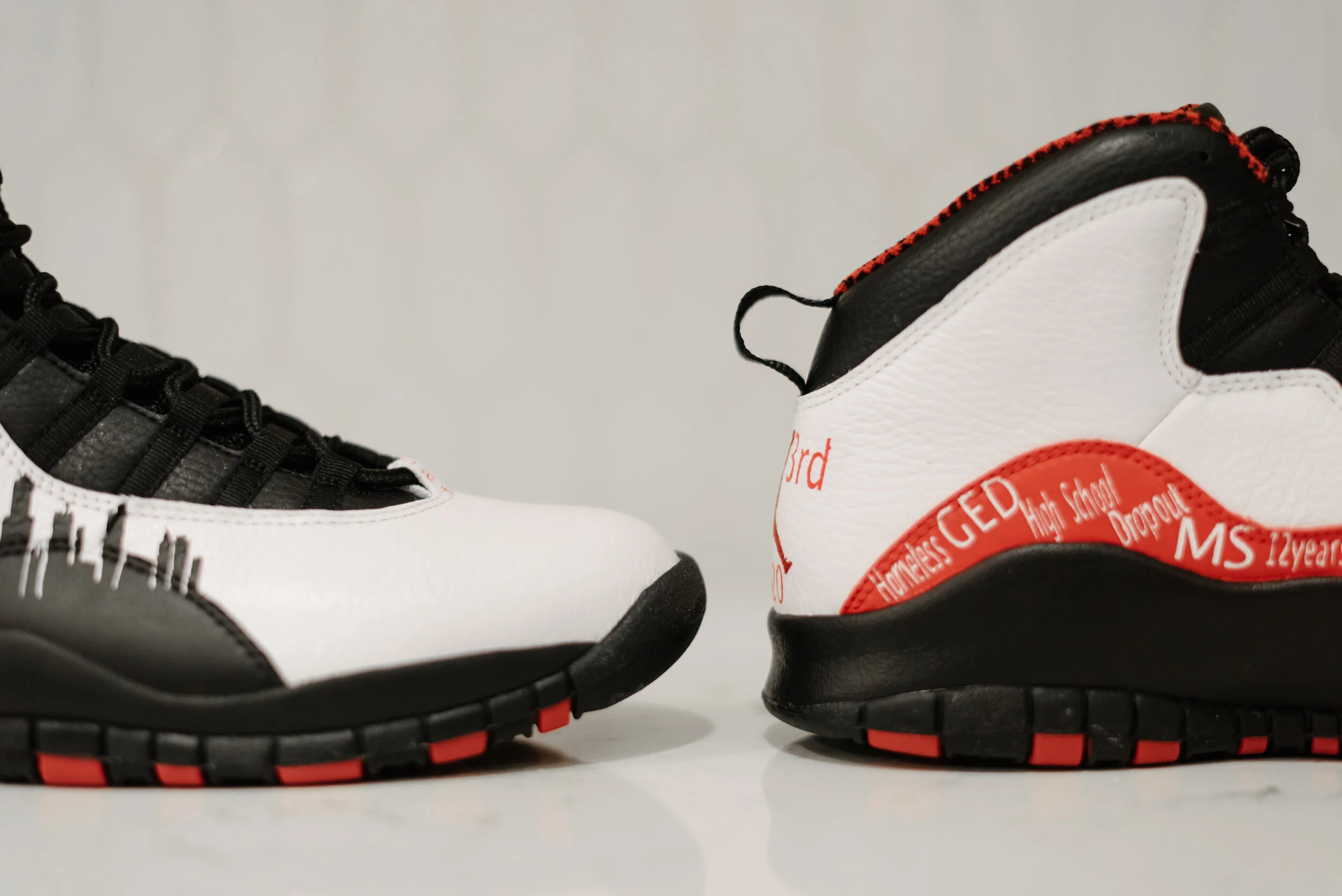 Pair of white and black sneakers with red accents, displaying school-related text and logos.