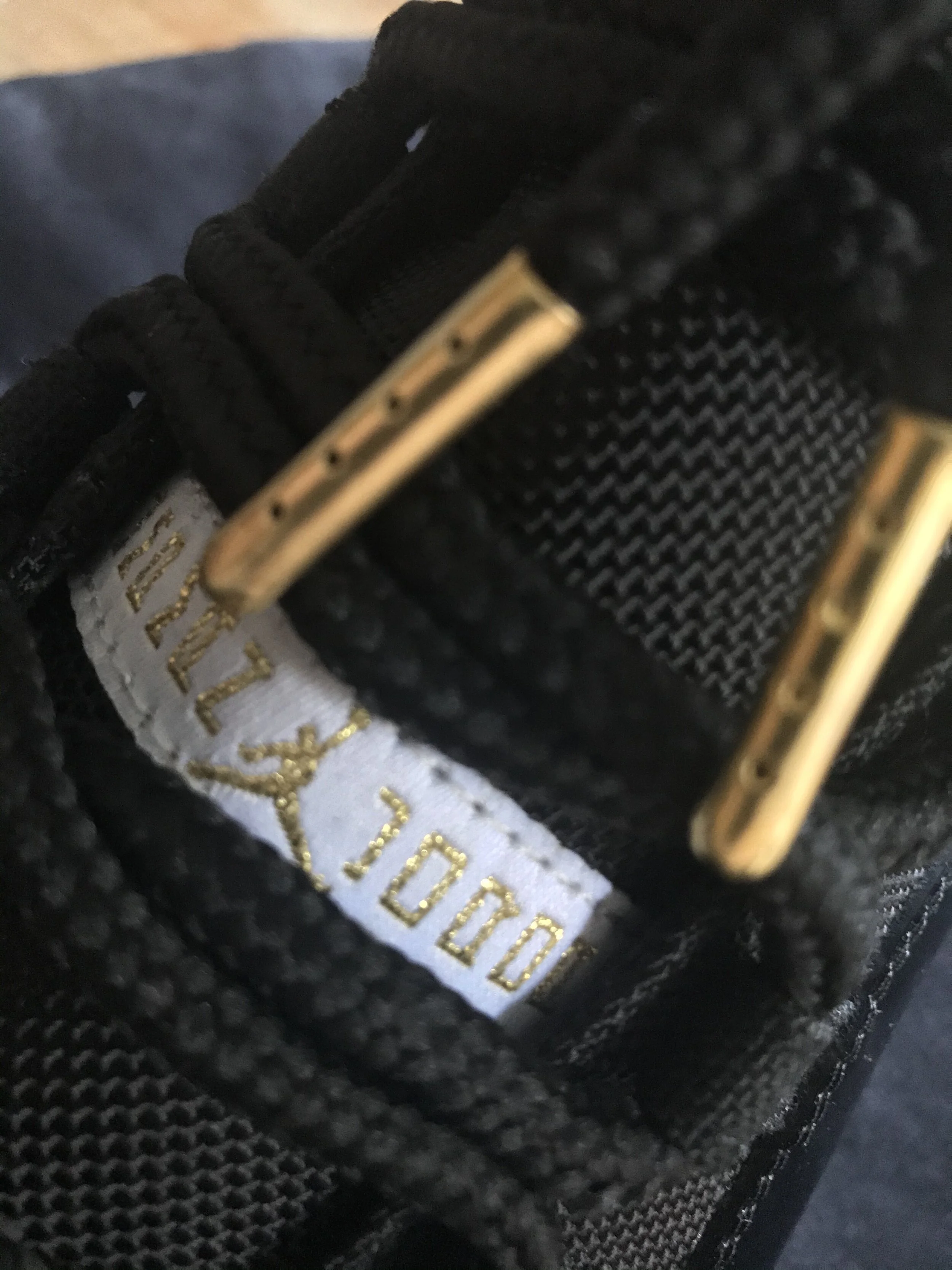 Close-up of the inside of a black sneaker showing a white label with gold text and the shoe size, alongside black and gold laces.