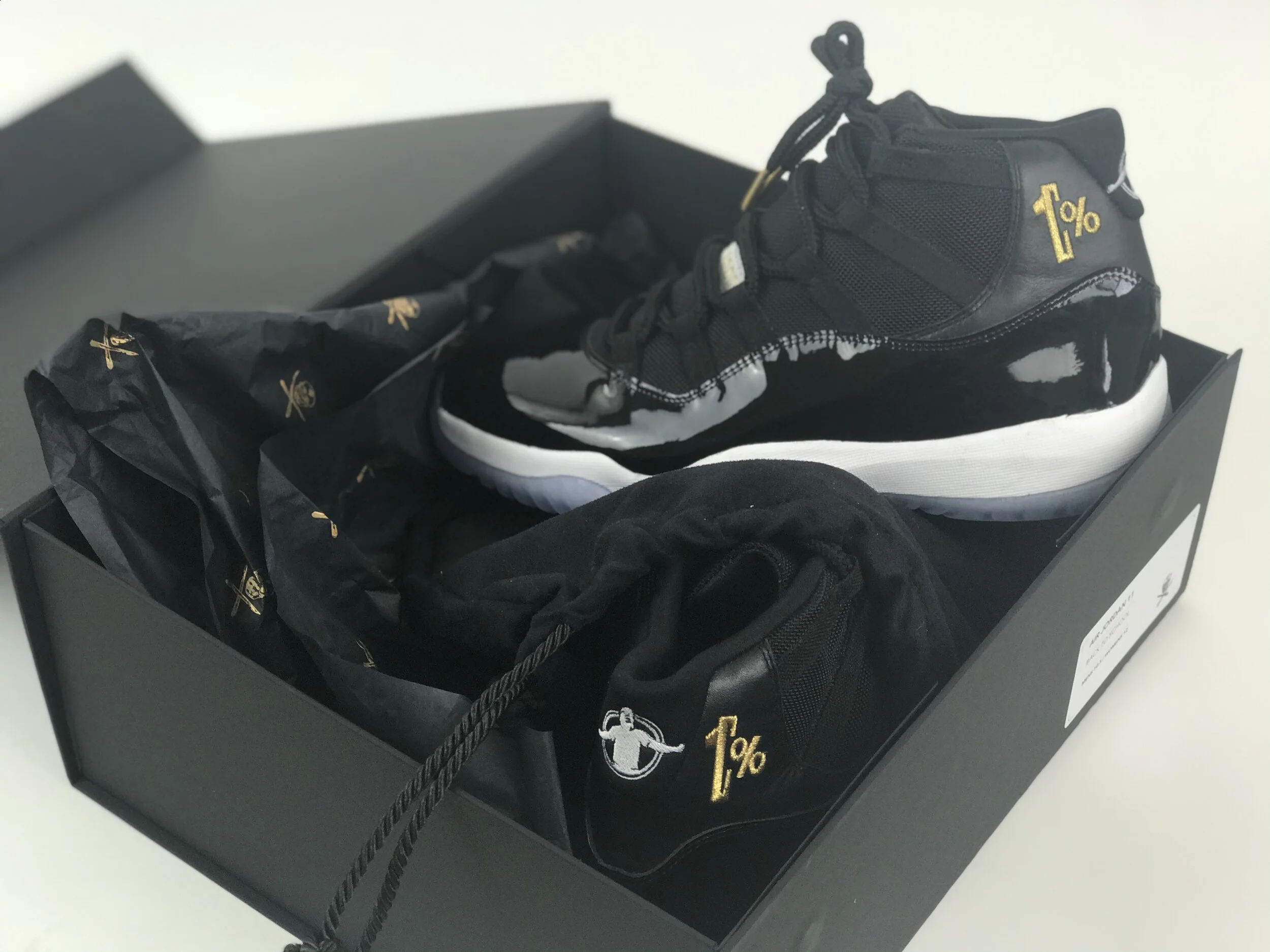 Black and white sneakers in a black shoe box with black tissue paper and packaging material