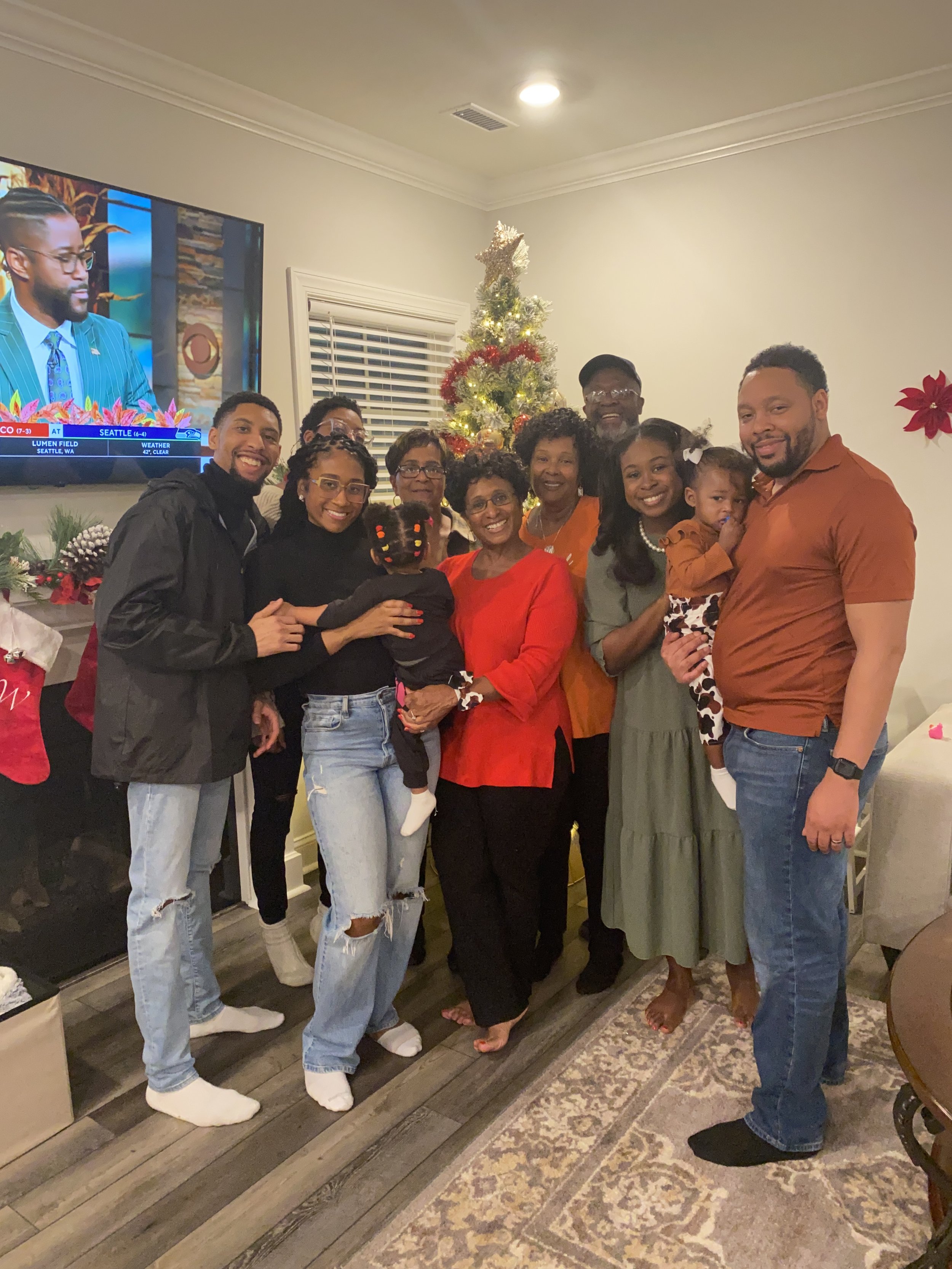A family gathering during Christmas with ten people posing together in front of a decorated Christmas tree. They are indoors with some wearing festive colors, smiling, and enjoying the holiday celebration.