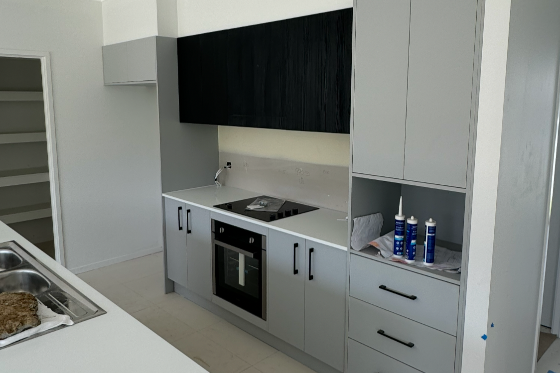 Modern kitchen with gray and black cabinets, a built-in oven, and countertop with kitchen tools and supplies.