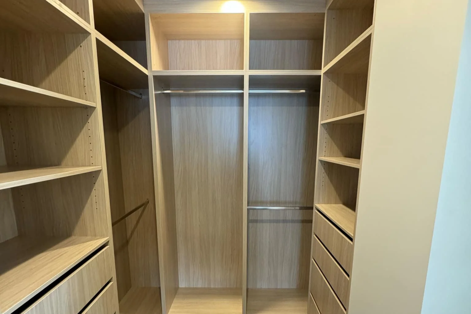 Empty wooden walk-in closet with shelves, drawers, and hanging rods.