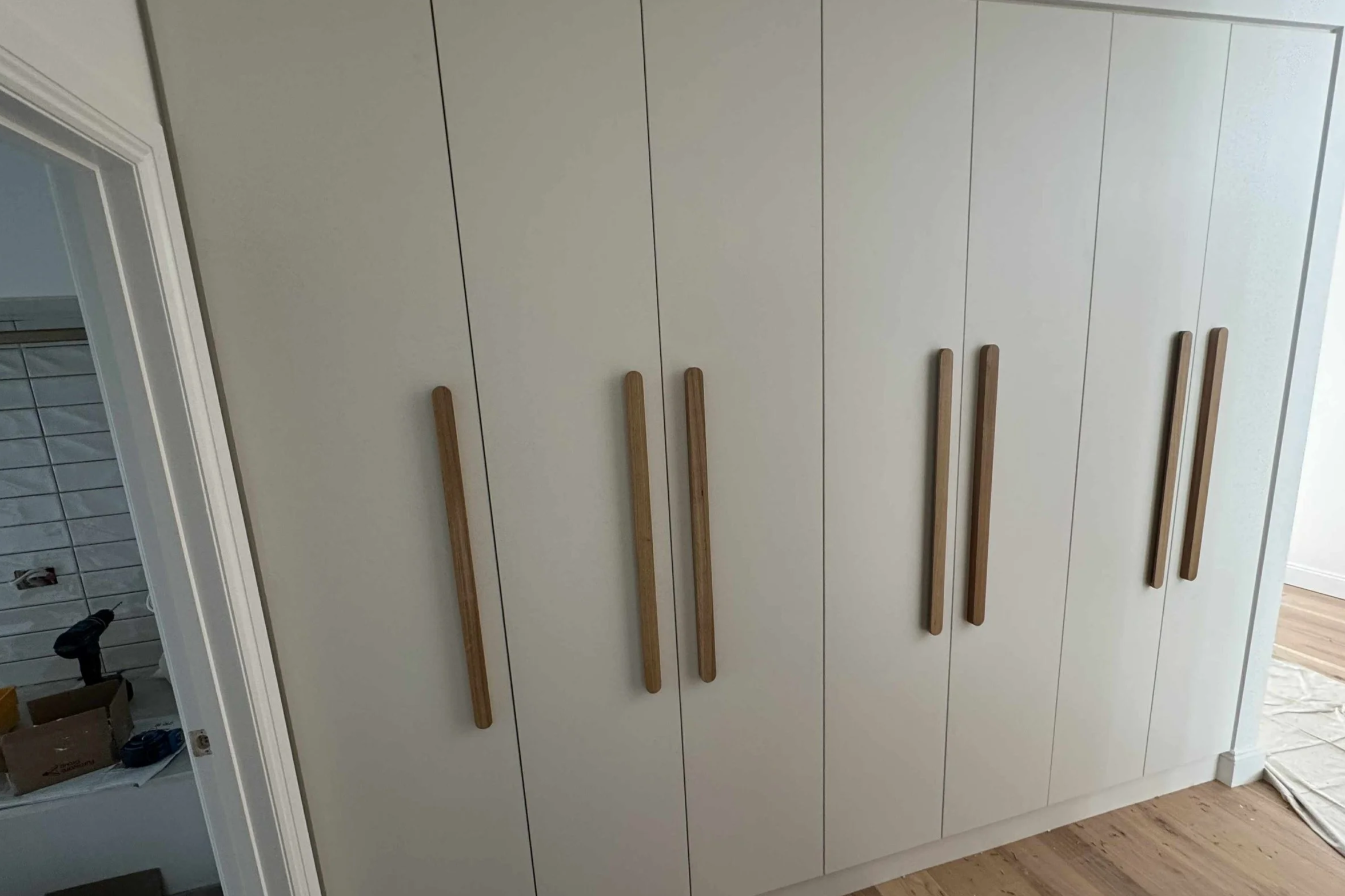 White wardrobe with wooden handles in a room with wooden floors.