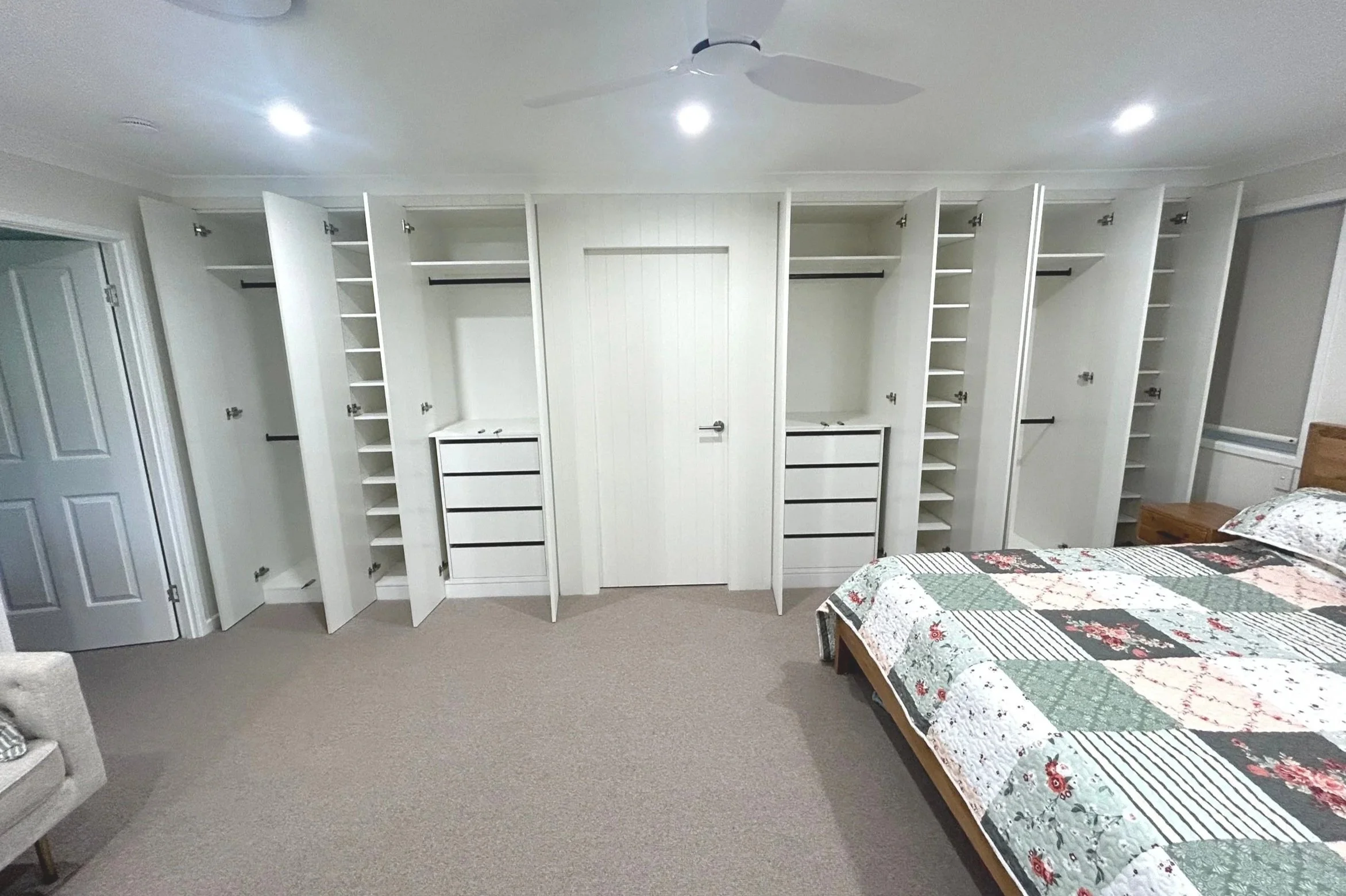 Bedroom with open white closets, a quilted bed, ceiling fan, chair, and modern lighting.