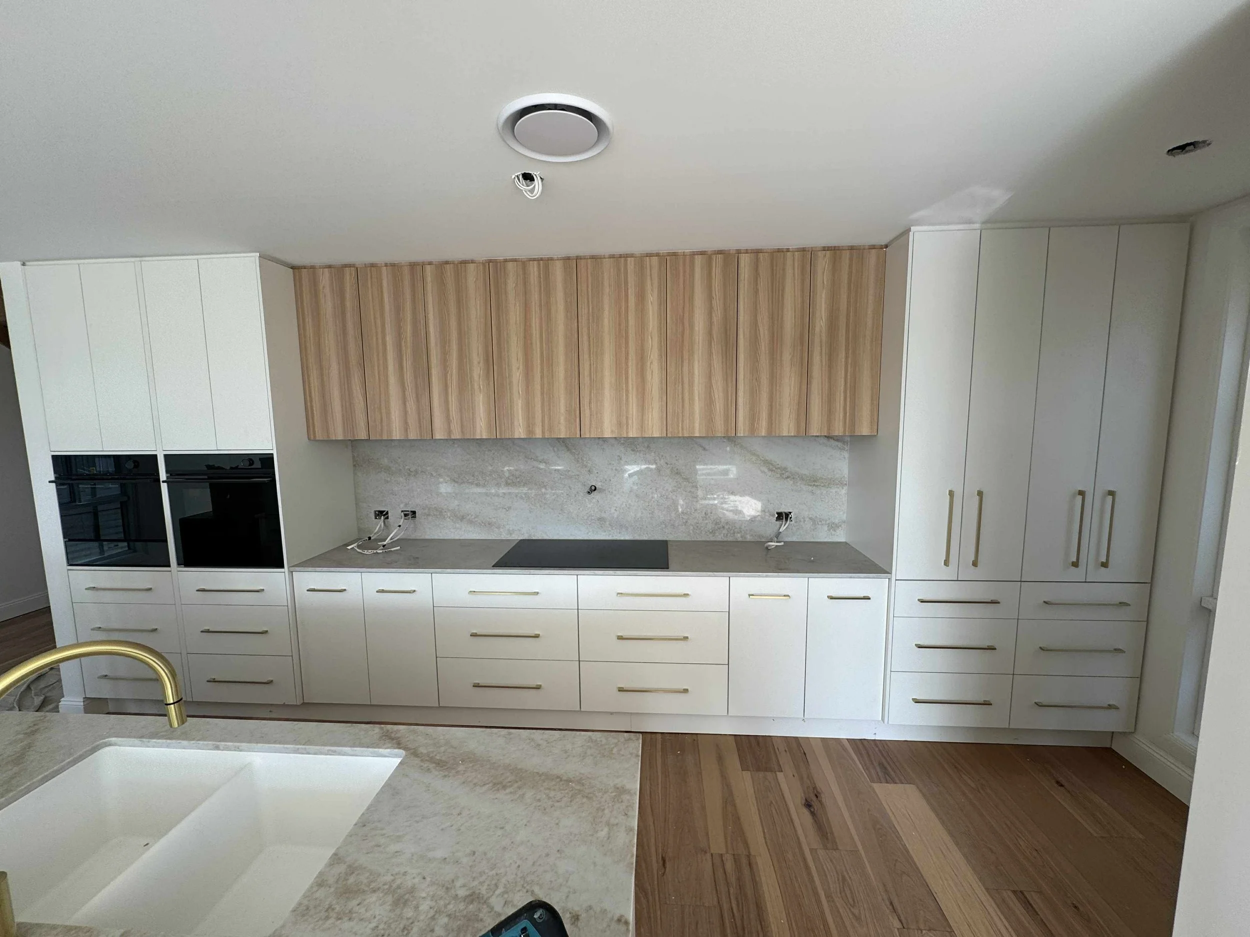 Modern kitchen with white cabinets, wooden upper cabinets, marble backsplash, hardwood flooring, and a kitchen island with a gold faucet.
