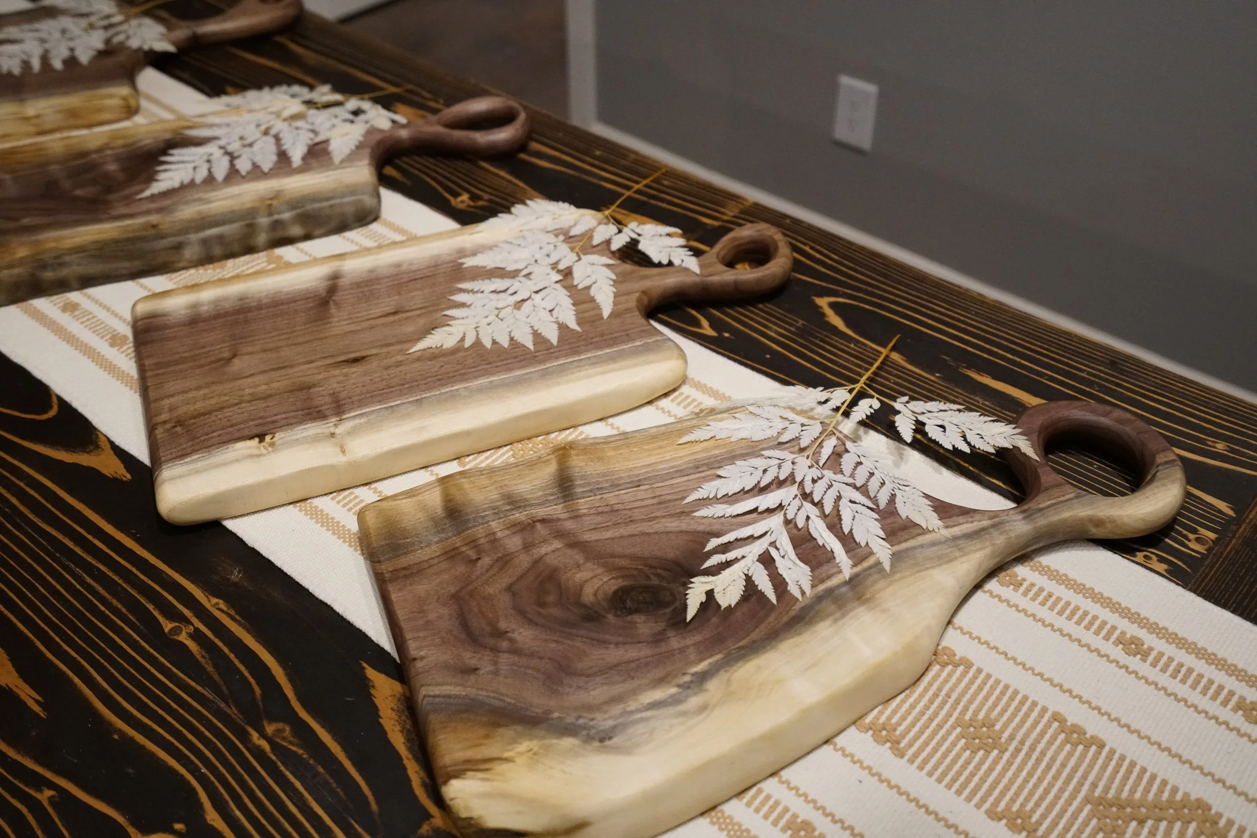 Three wooden cutting boards with carved leaf patterns are arranged on a table with a patterned tablecloth.