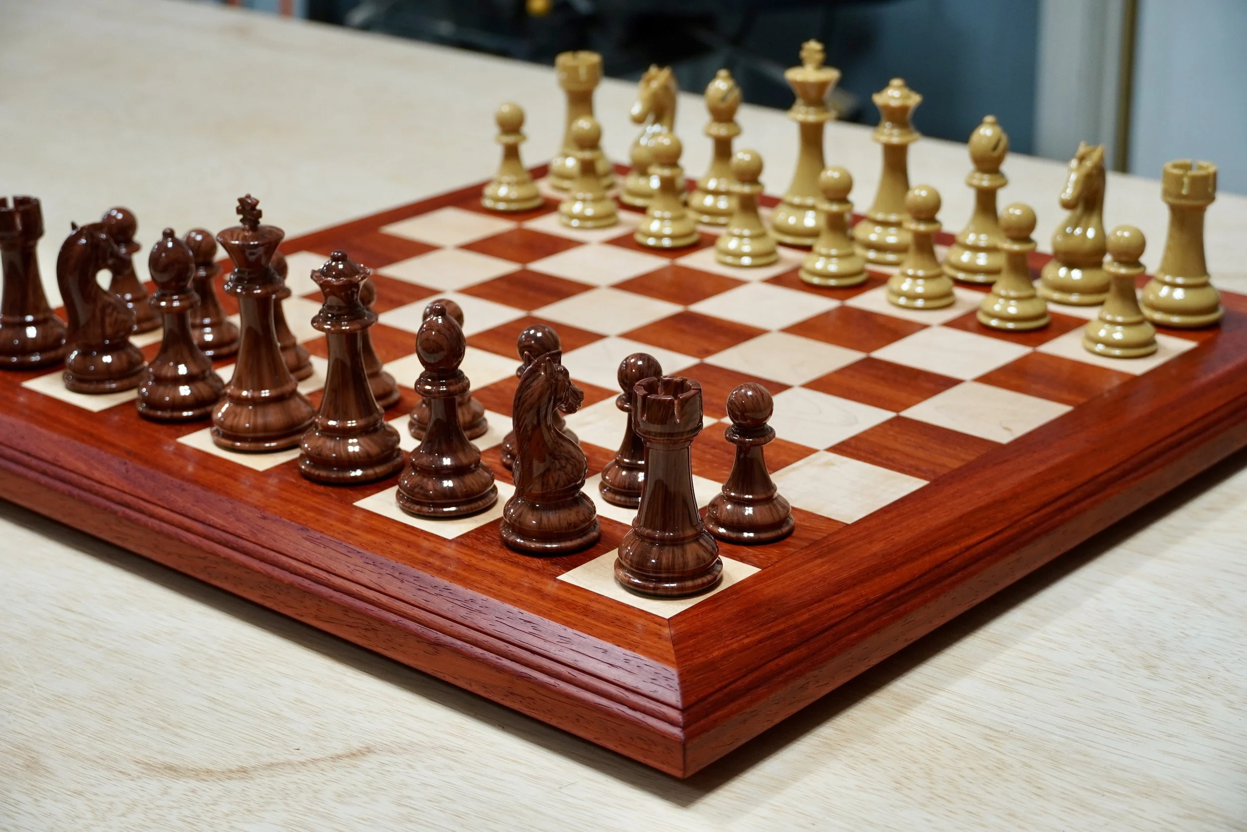 A chessboard set up for a game with wooden chess pieces on a light-colored table.