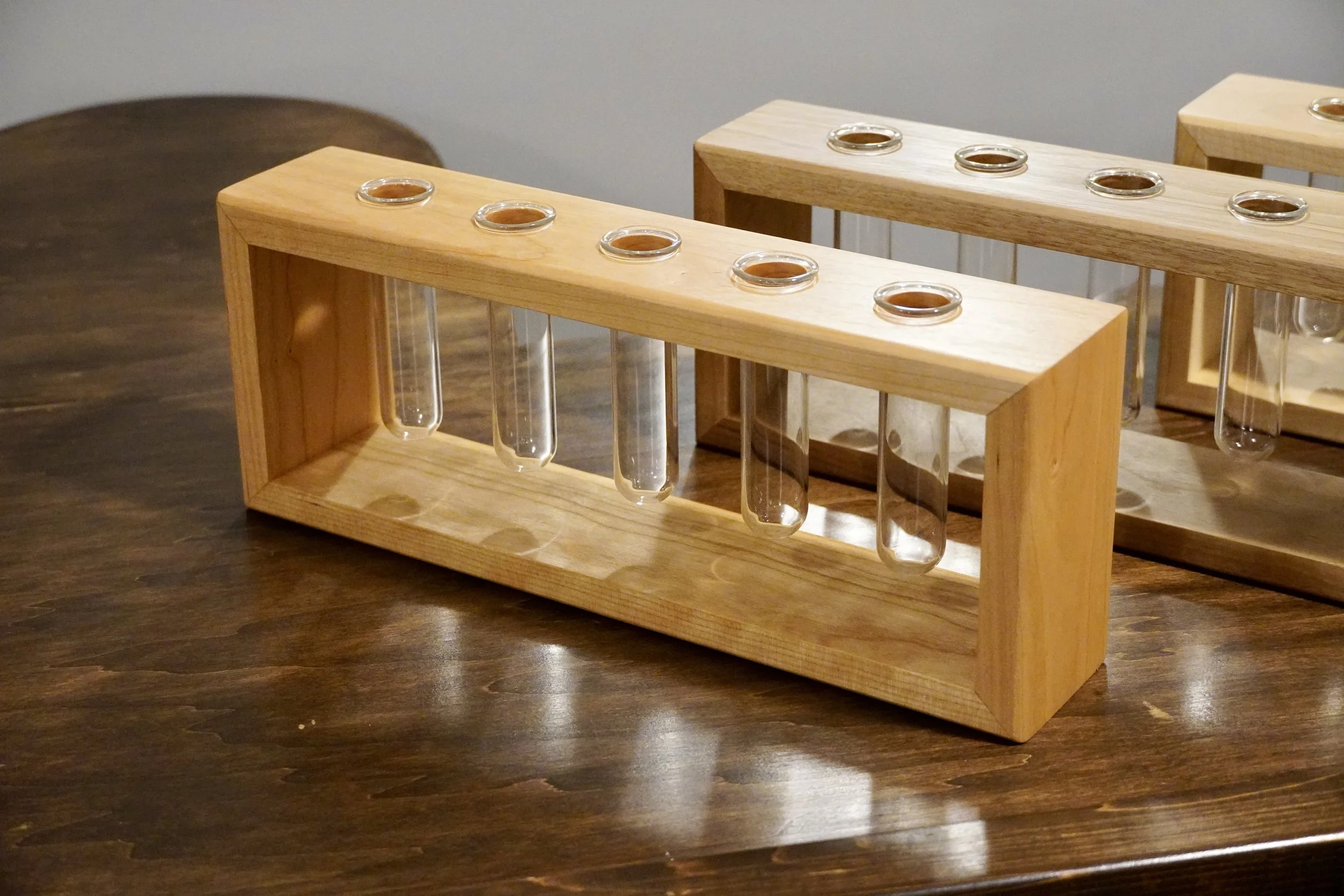 Wooden test tube holder with glass test tubes containing a brown liquid on a wooden table.
