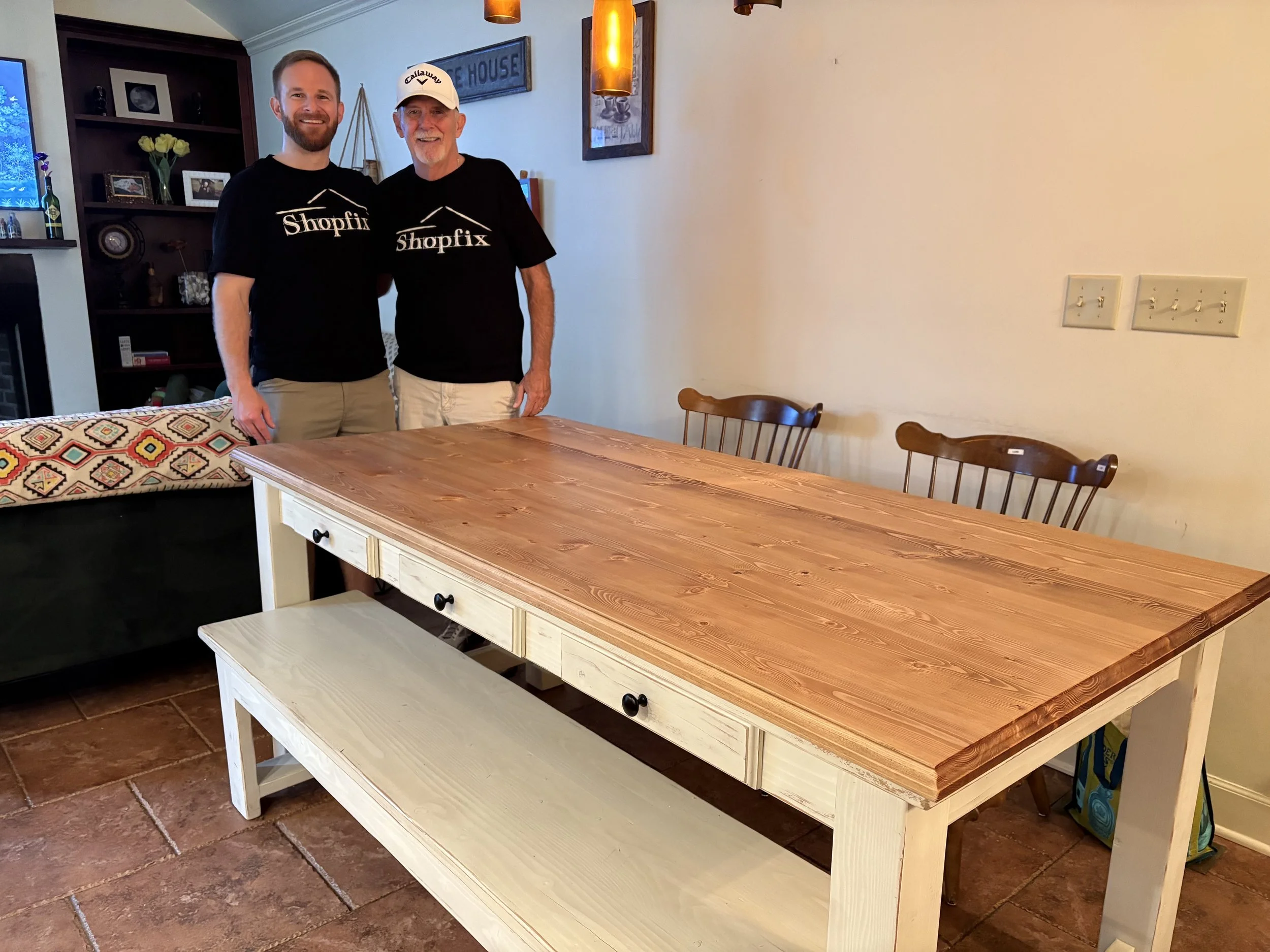Two men standing behind a large wooden dining table in a room.