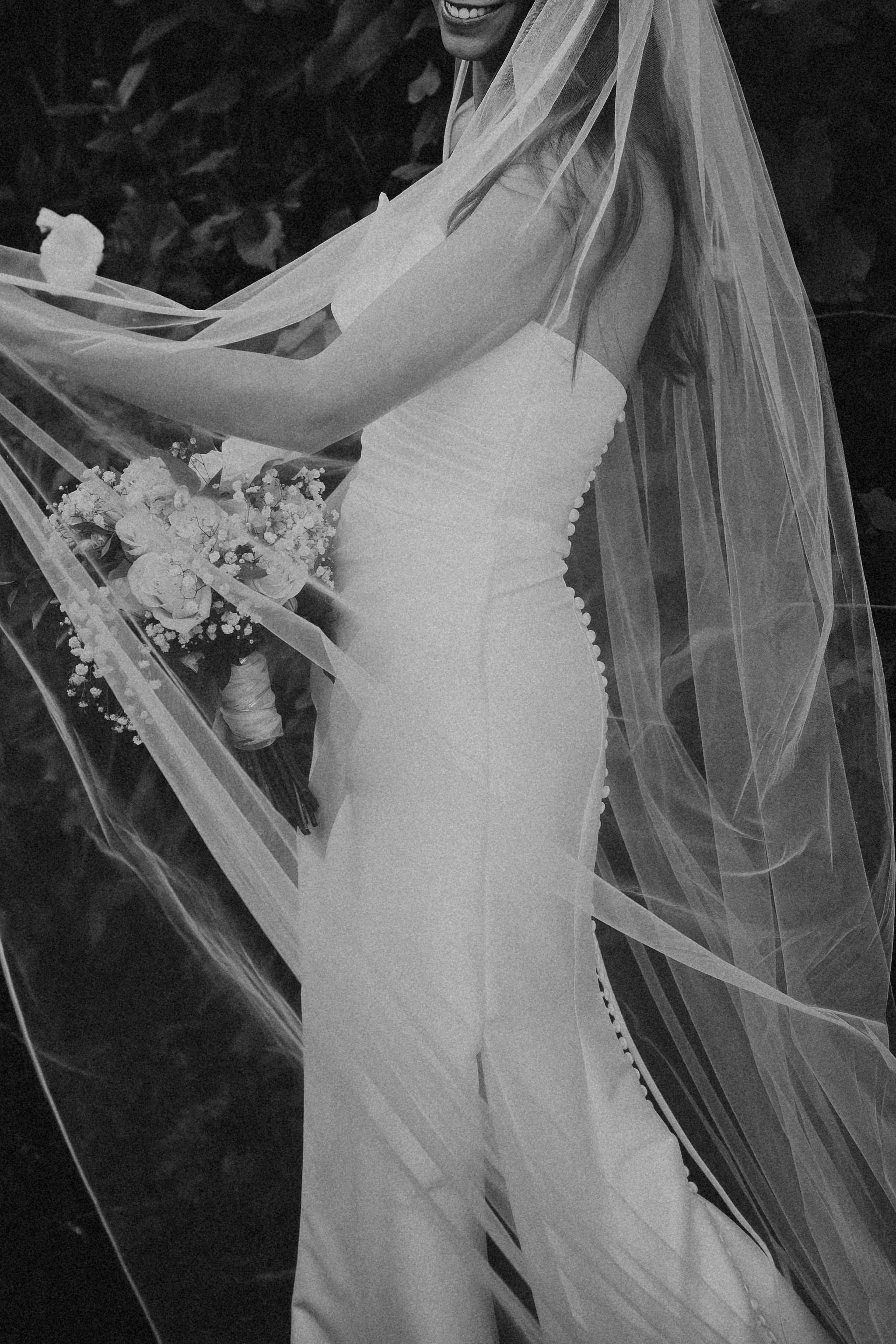 A bride in a strapless wedding gown with a long veil, holding a bouquet of flowers, smiling.