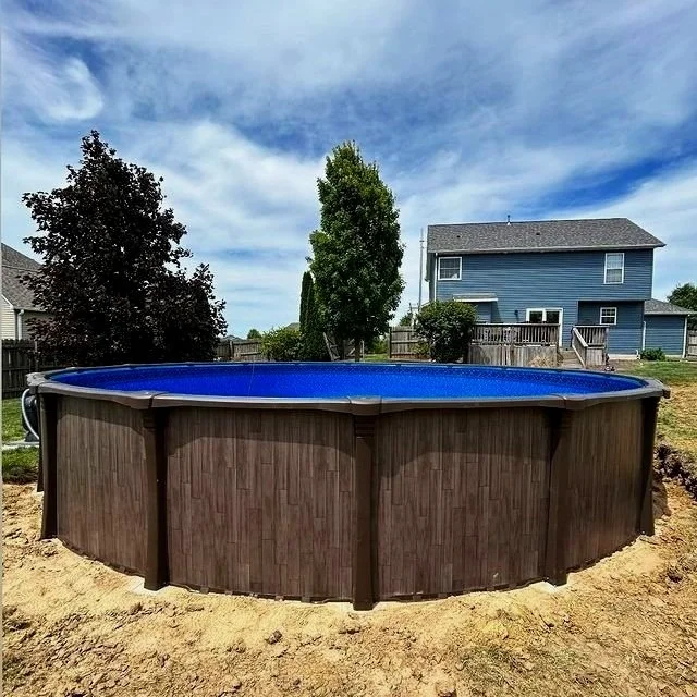 Above-ground pool in backyard with house and trees, under a cloudy sky.