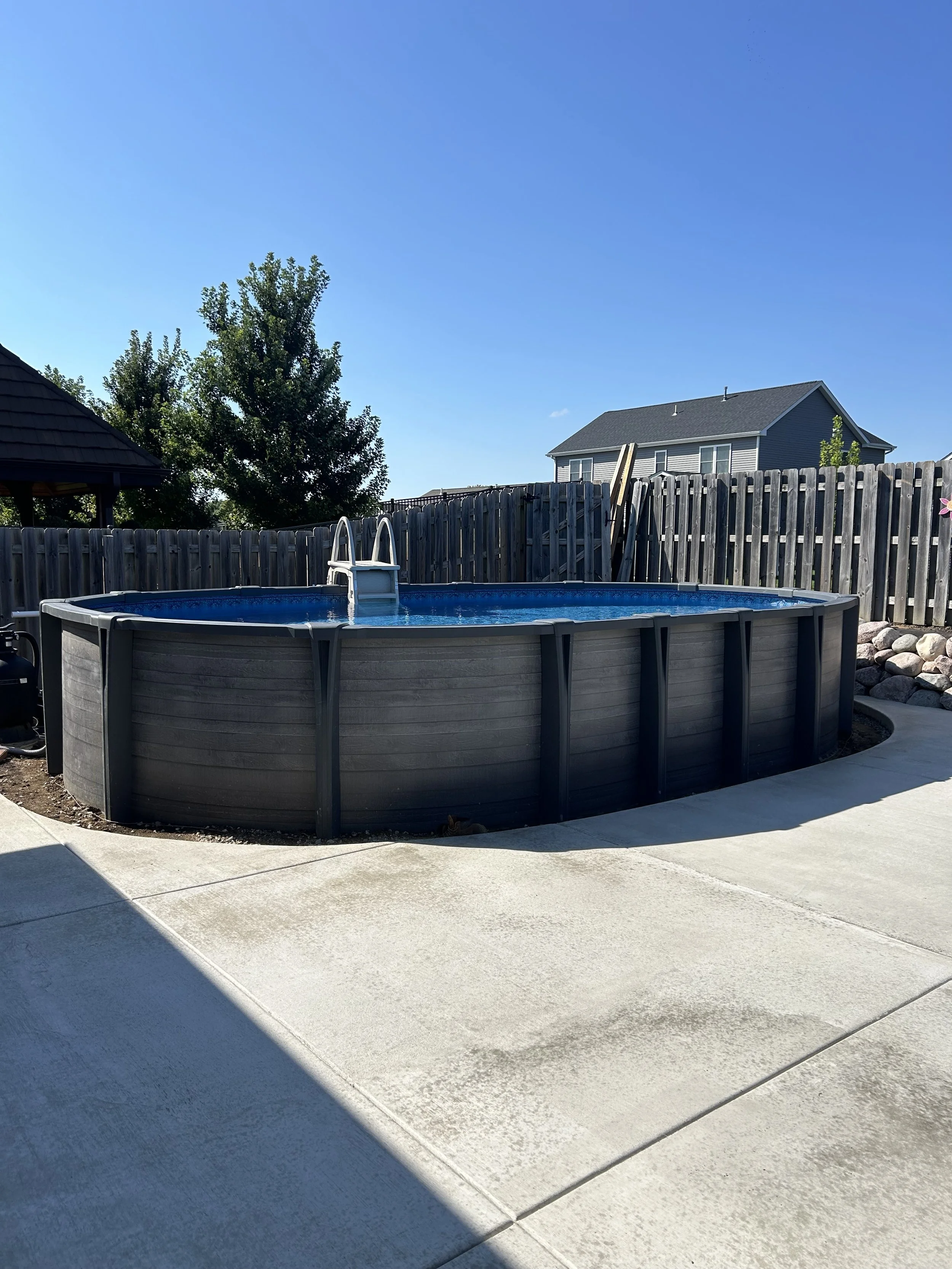 Above ground pool with ladder in a backyard surrounded by a wooden privacy fence.