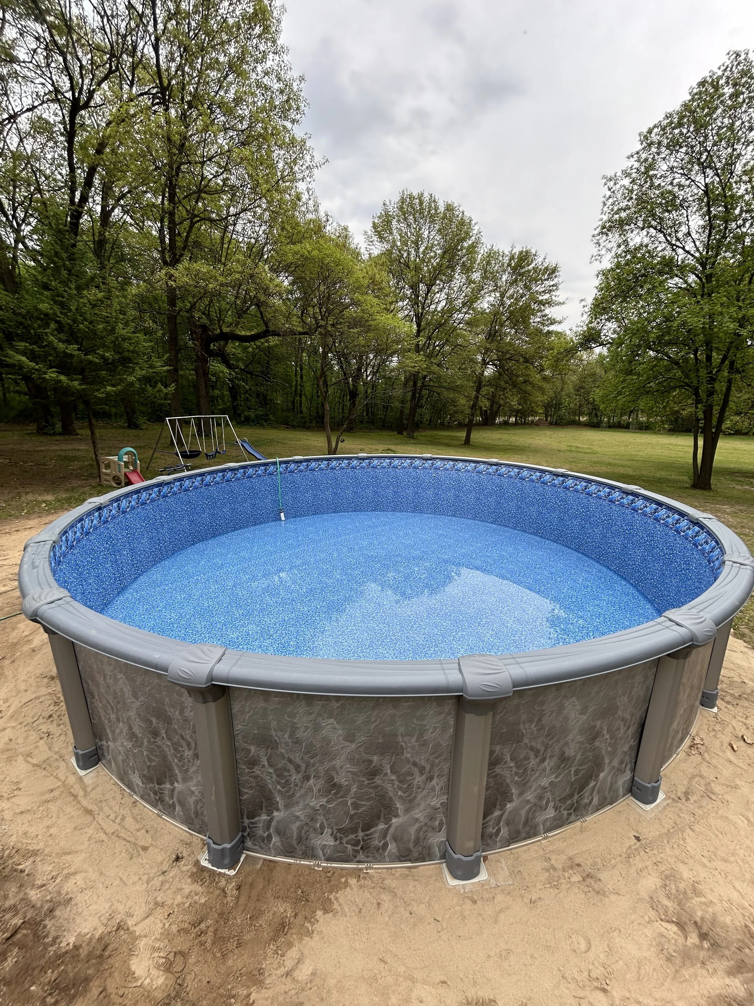 Above-ground swimming pool in a backyard with surrounding trees and greenery.
