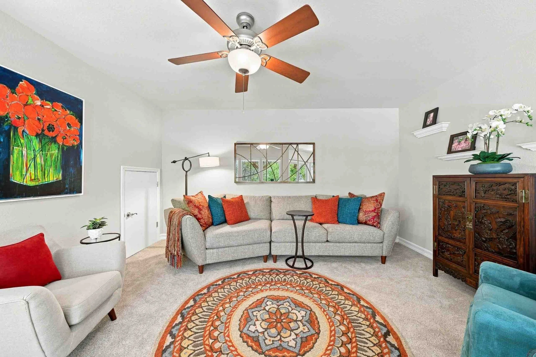 Colorful sitting room with a sectional sofa, patterned rug, ceiling fan, and decorative furnishings.