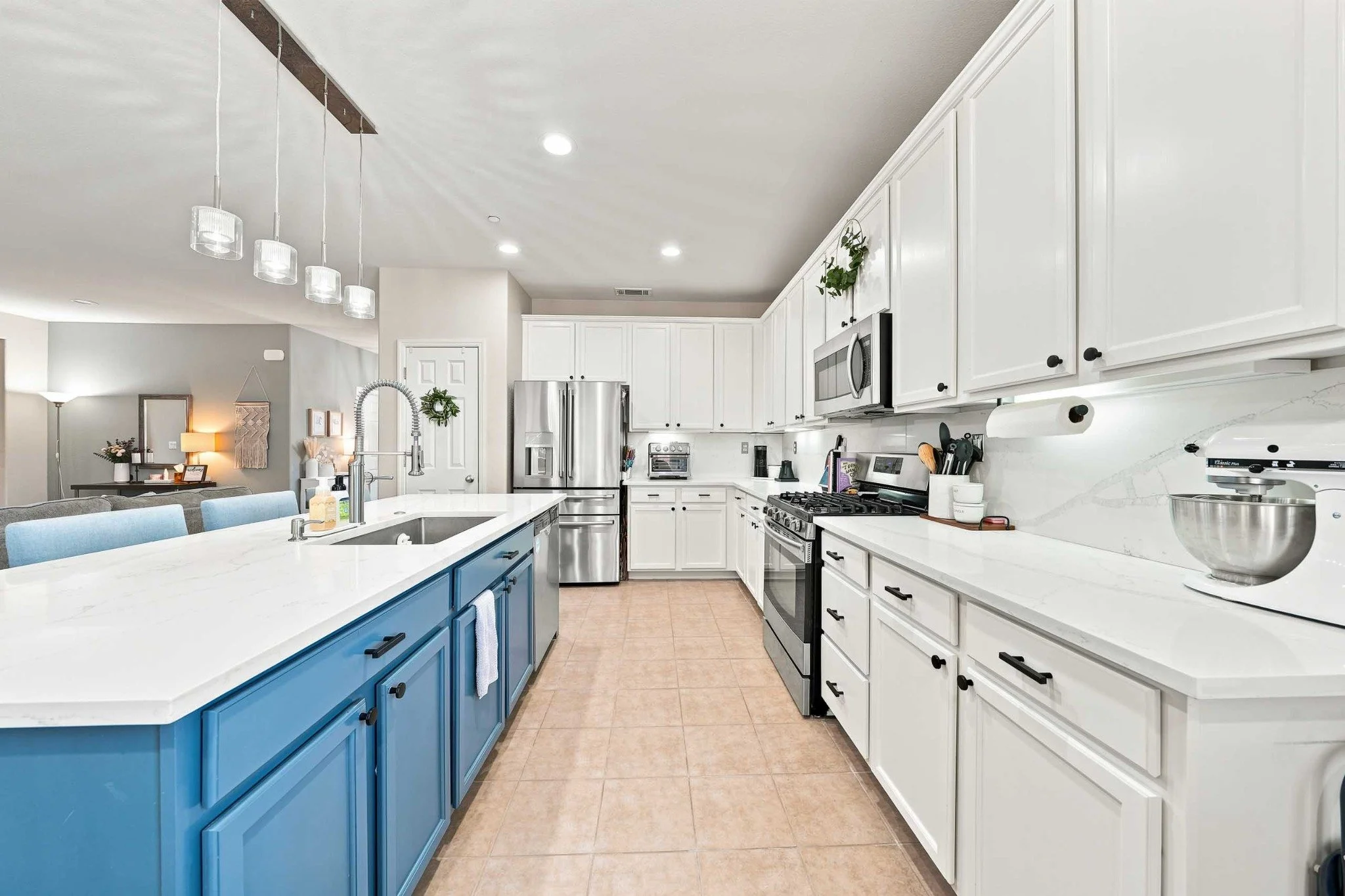 Bright white kitchen with a blue island, quartz counters, stainless appliances, and pendant lights.