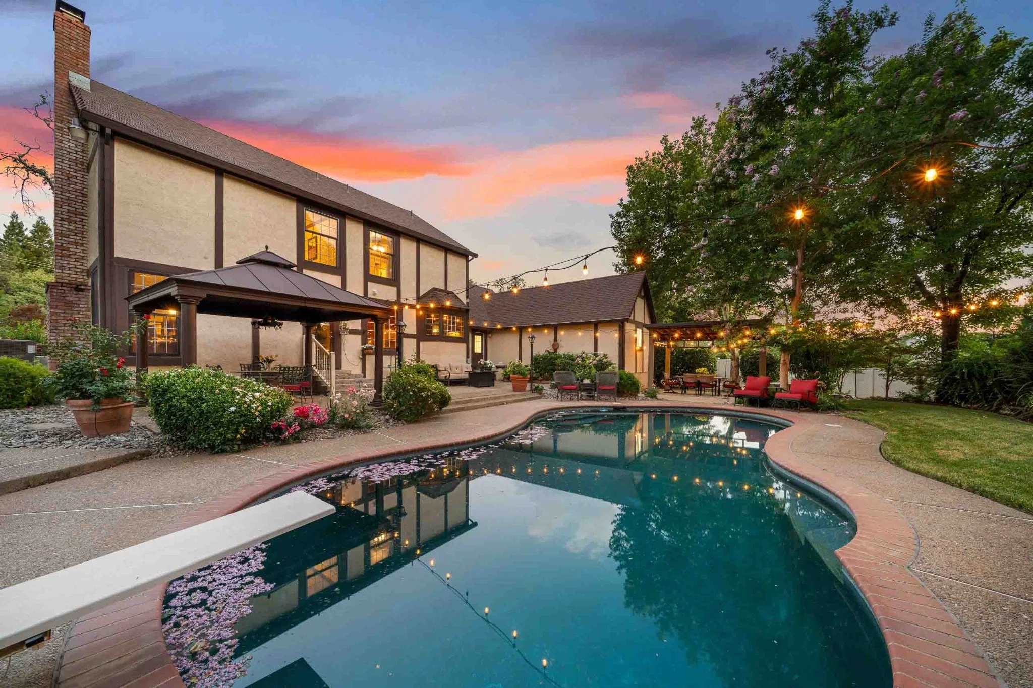 Luxury home backyard with a swimming pool, patio seating, string lights, and a colorful twilight sky.