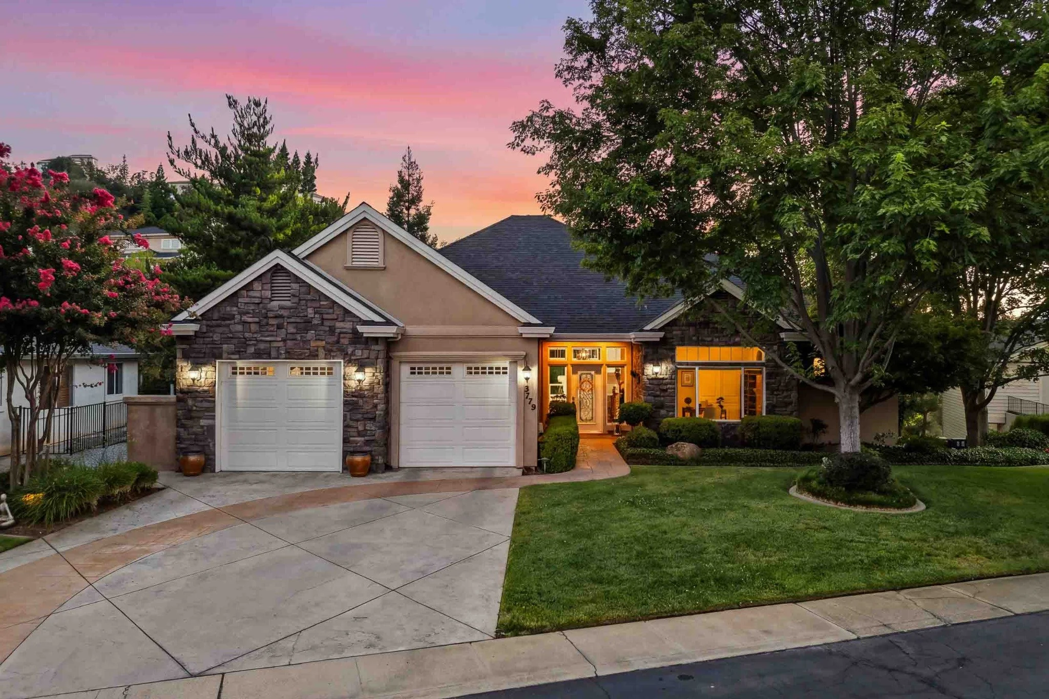 Luxury home exterior with stone accents, mature landscaping, and warm lighting at twilight in Redding.