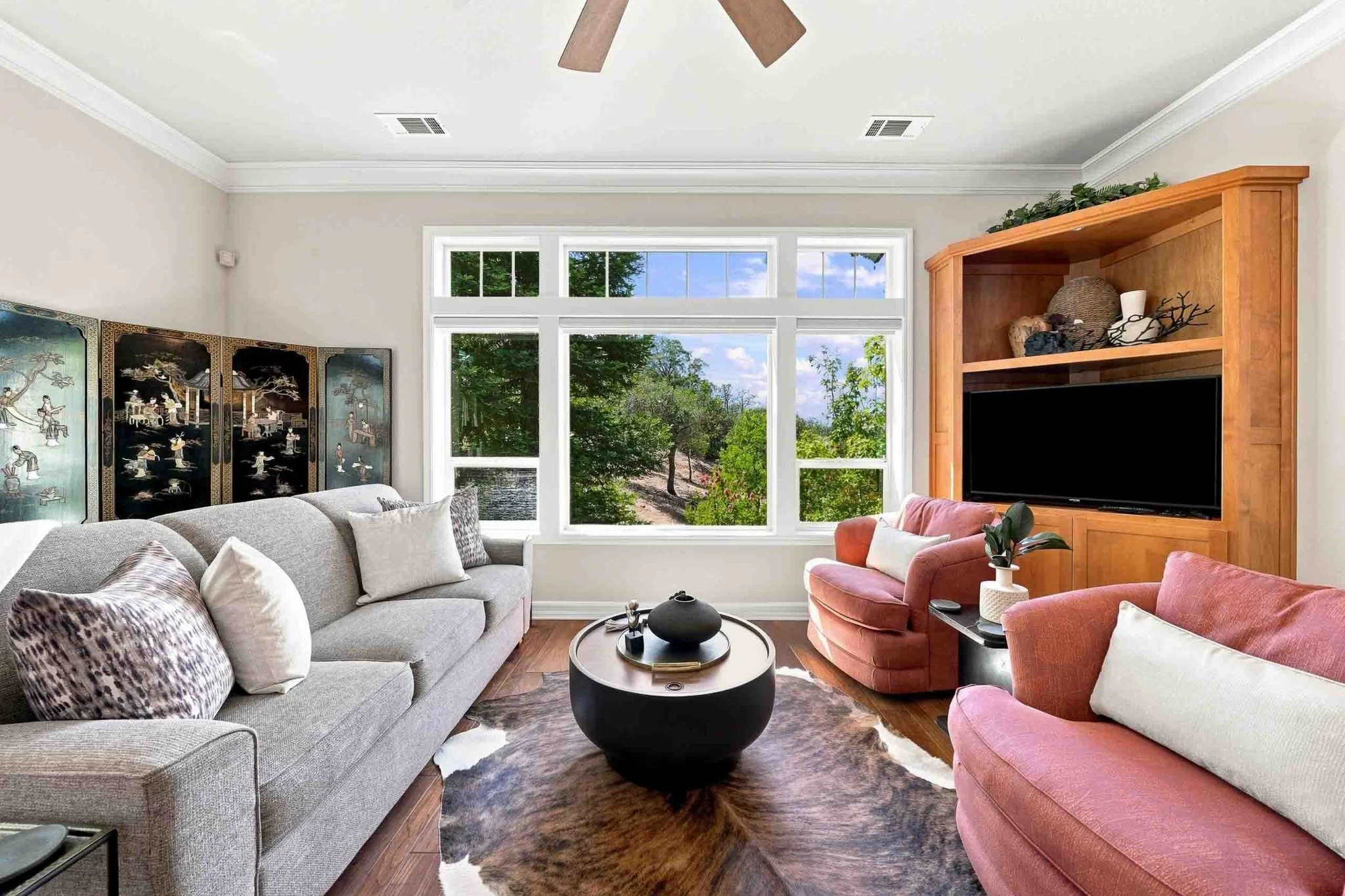 Bright family room with a gray sofa, colorful chairs, wood flooring, and a built-in media cabinet.