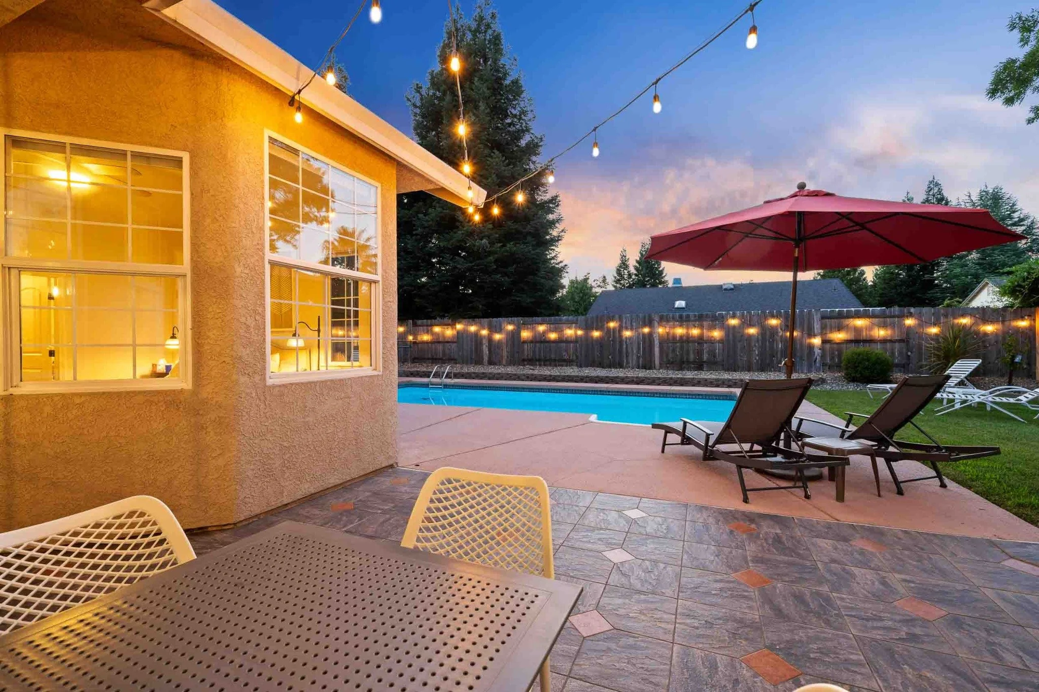 Backyard patio and swimming pool with string lights at twilight in Redding, California.