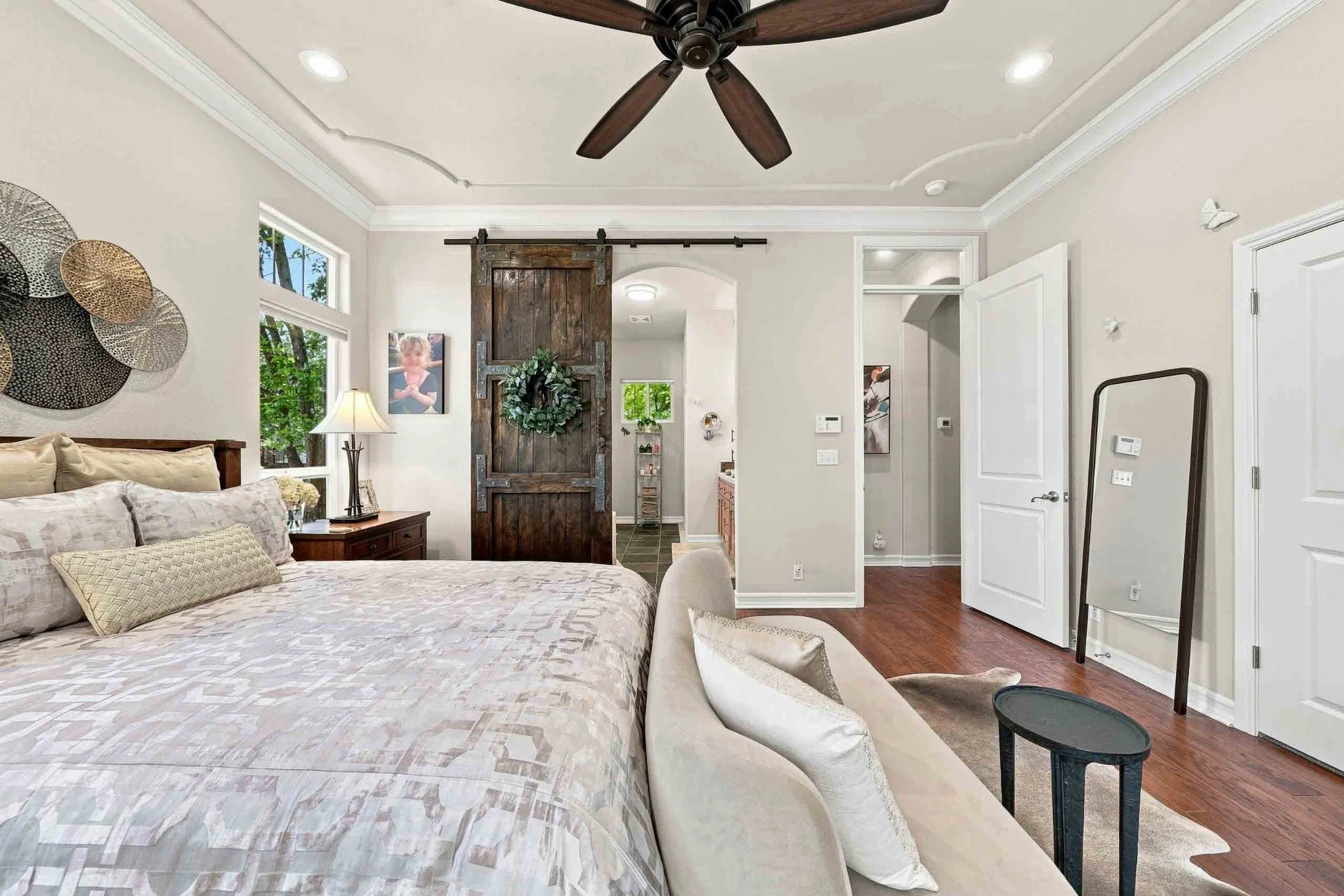 Primary bedroom with hardwood flooring, a rustic sliding barn door, and an adjoining bathroom.