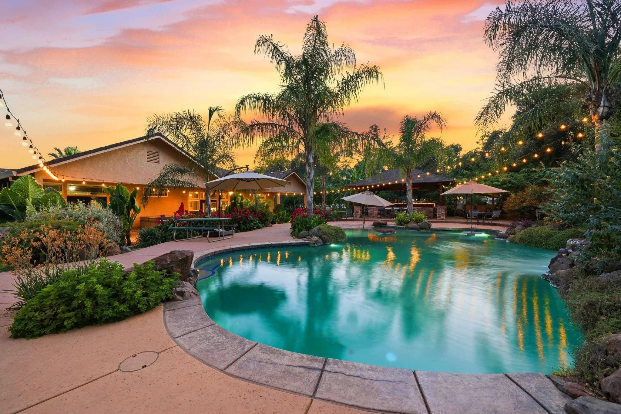 Luxury backyard swimming pool with palm trees, string lights, and a colorful sunset in Redding, California.