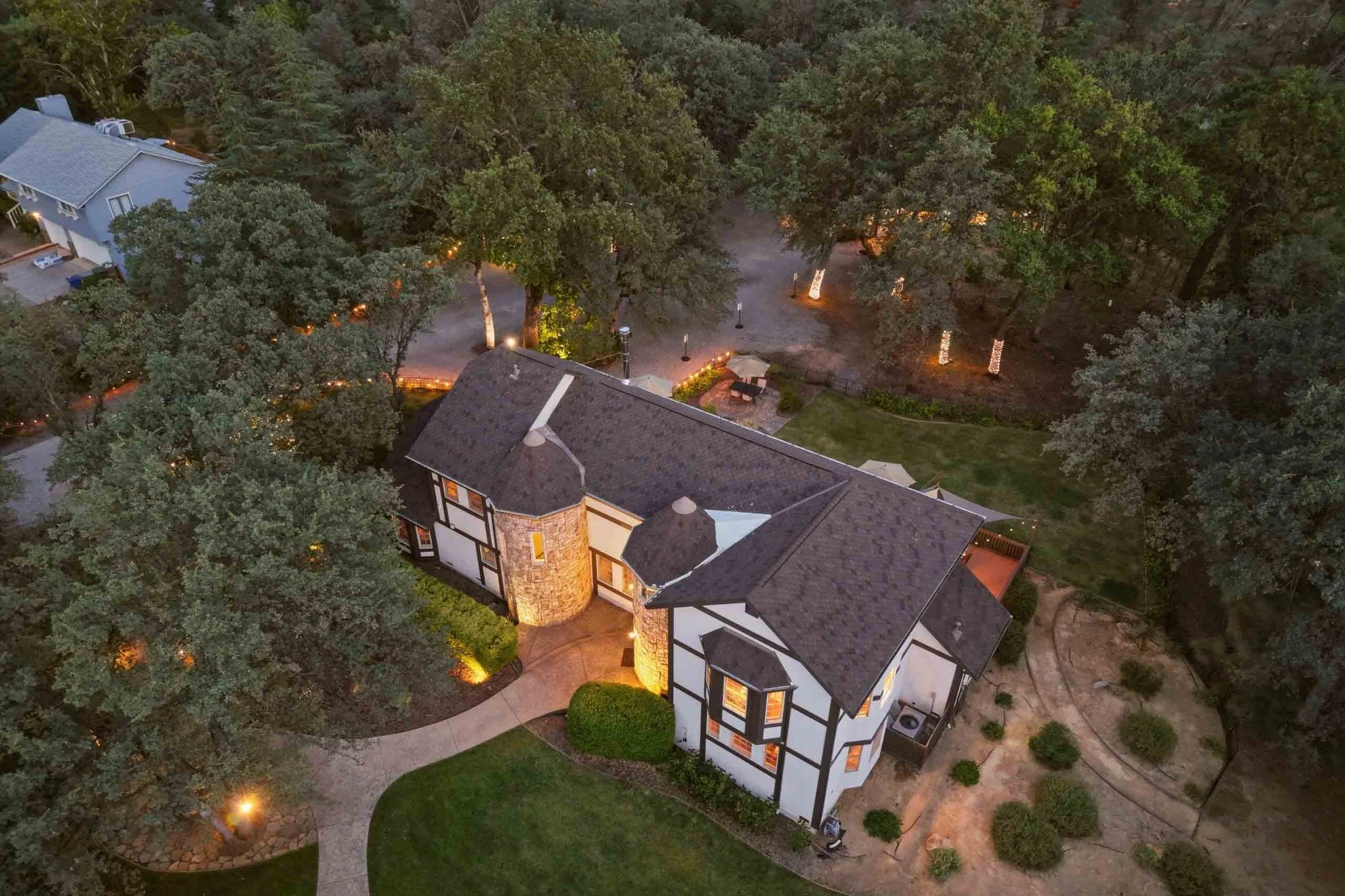 Aerial twilight view of a luxury home surrounded by mature trees and landscape lighting in Redding, California.