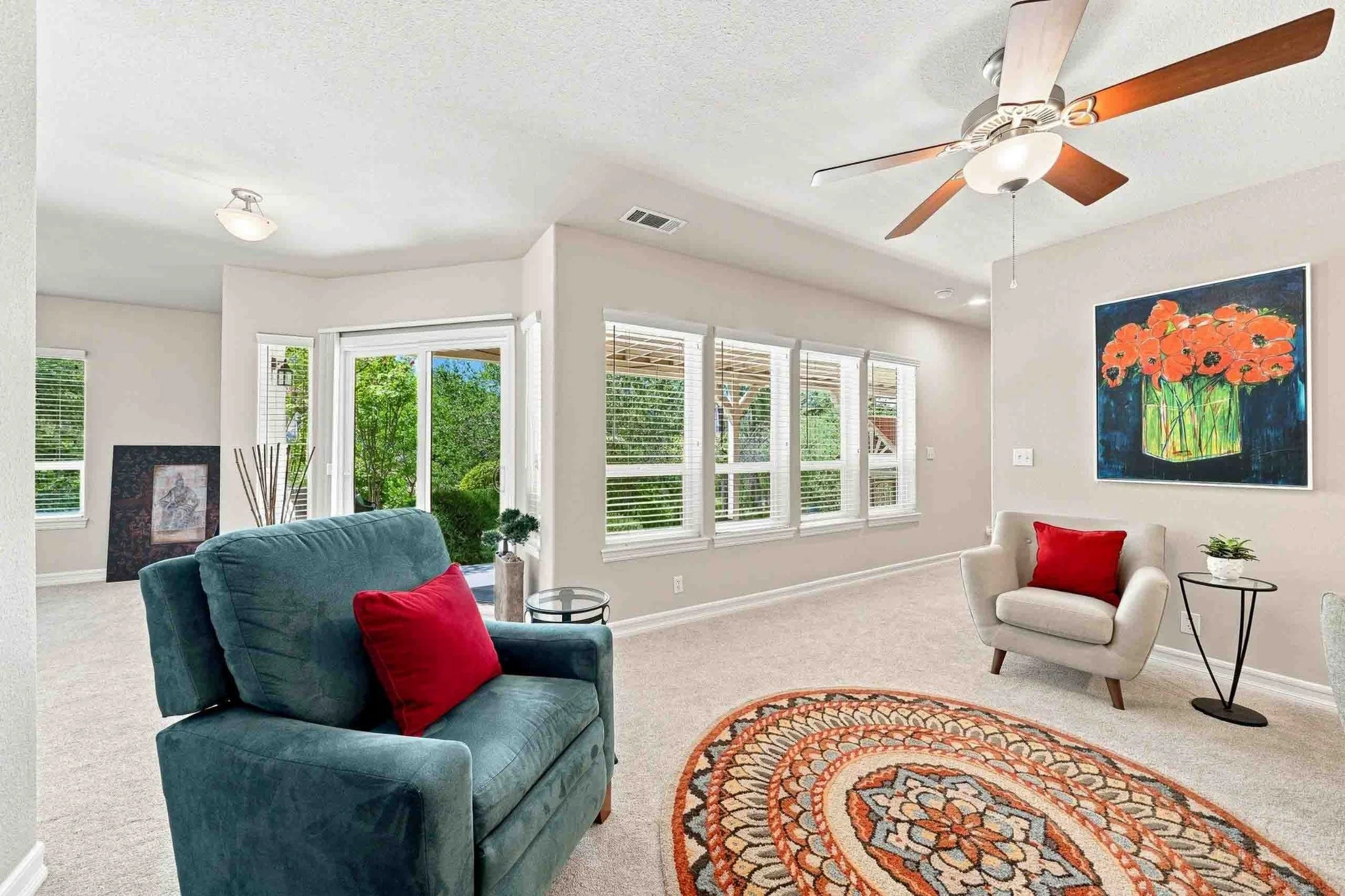 Bright sitting room with upholstered chairs, a patterned rug, large windows, and garden access.