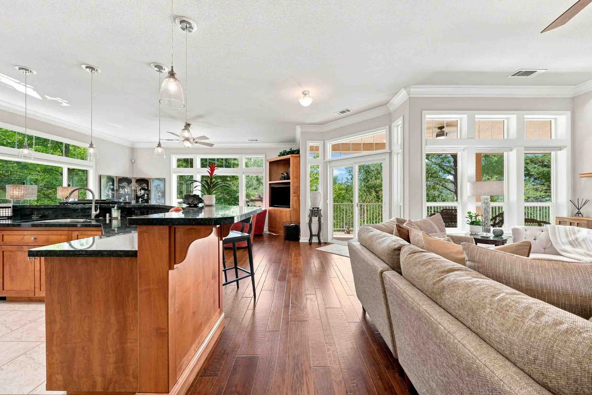 Open-concept kitchen and living area with wood cabinetry, dark counters, large windows, and hardwood floors.