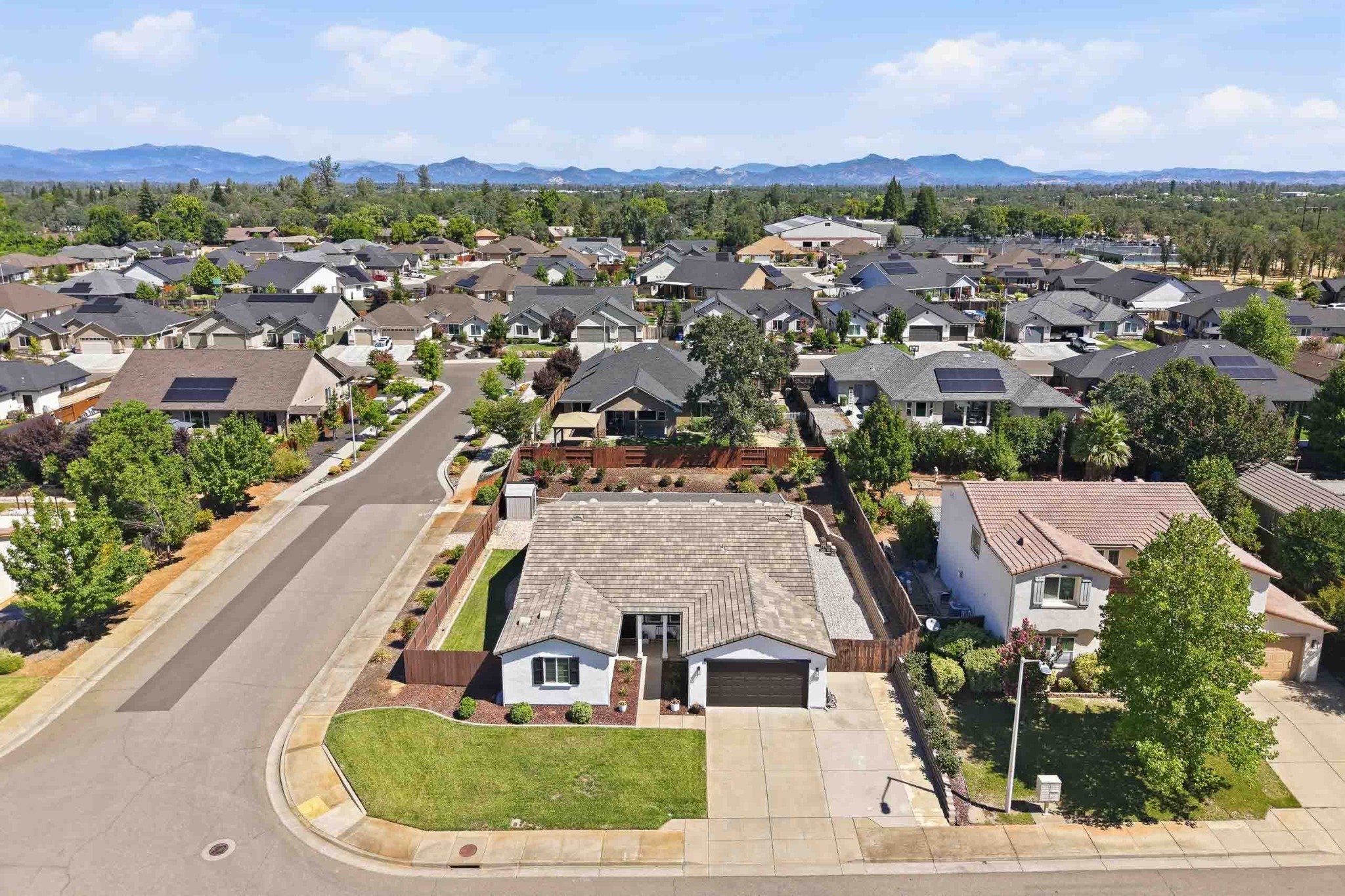 Aerial view of a Redding home within a residential neighborhood with mountain scenery beyond.