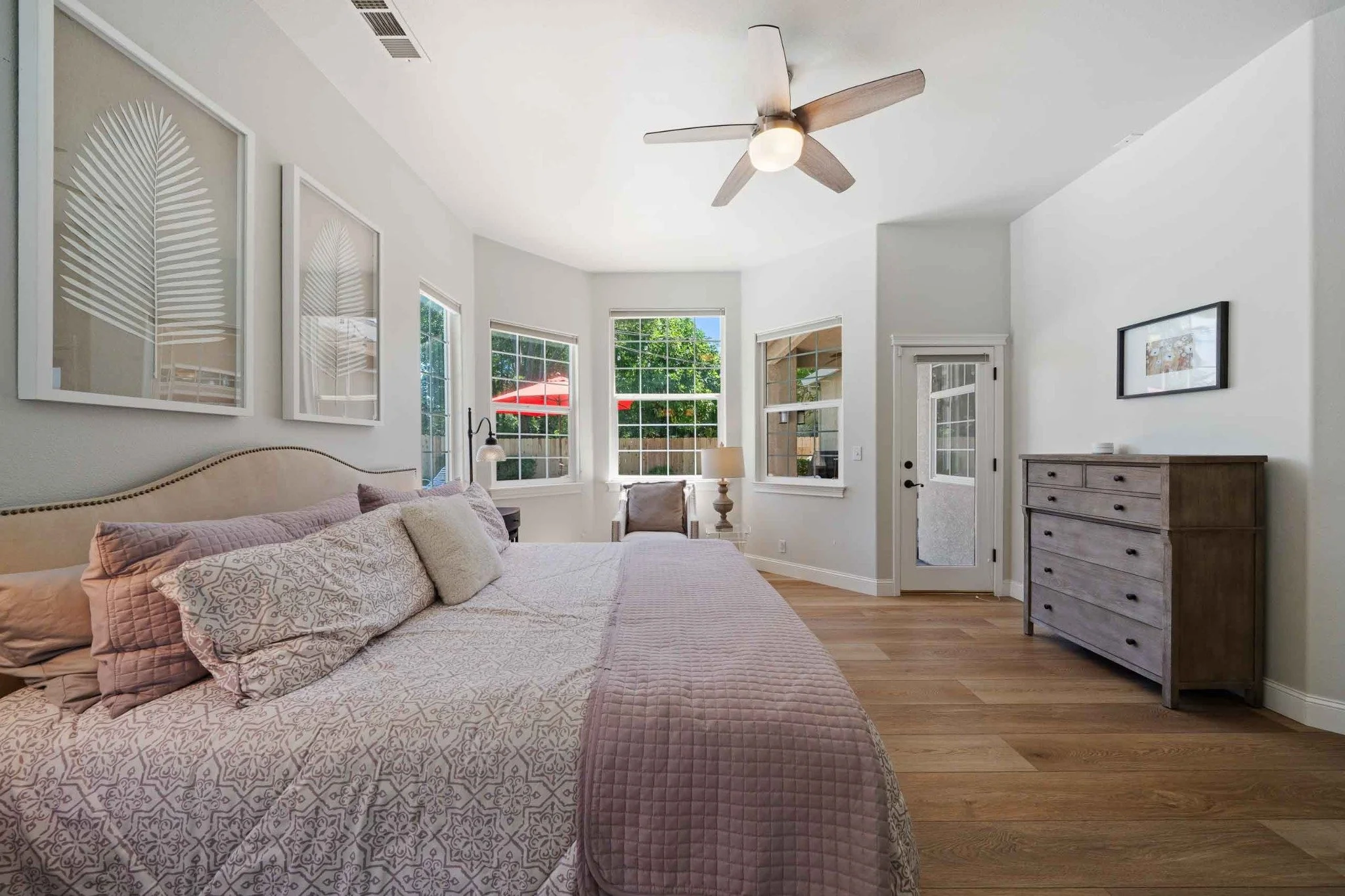 Spacious primary bedroom with multiple windows, wood flooring, and a ceiling fan.