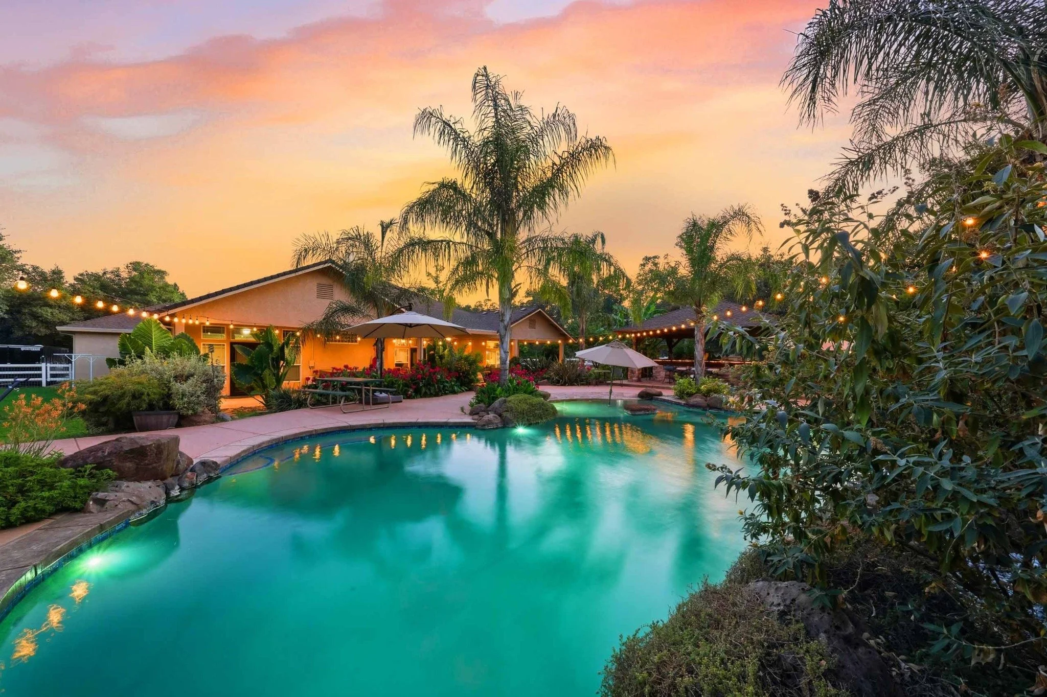 Resort-style backyard pool with palm trees and landscape lighting at sunset in Redding, California.