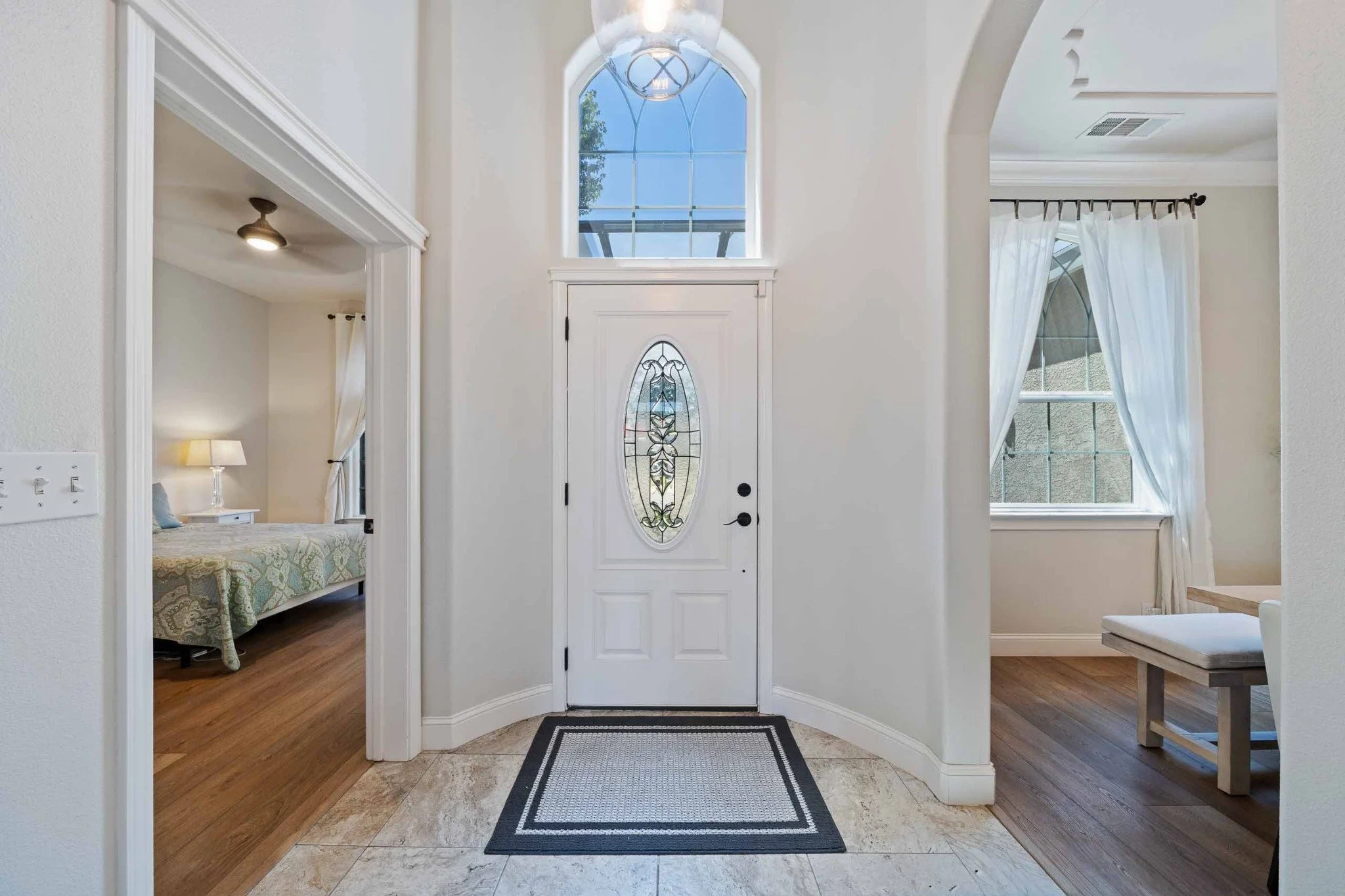Bright home entryway with an arched opening, decorative front door, and adjoining rooms.