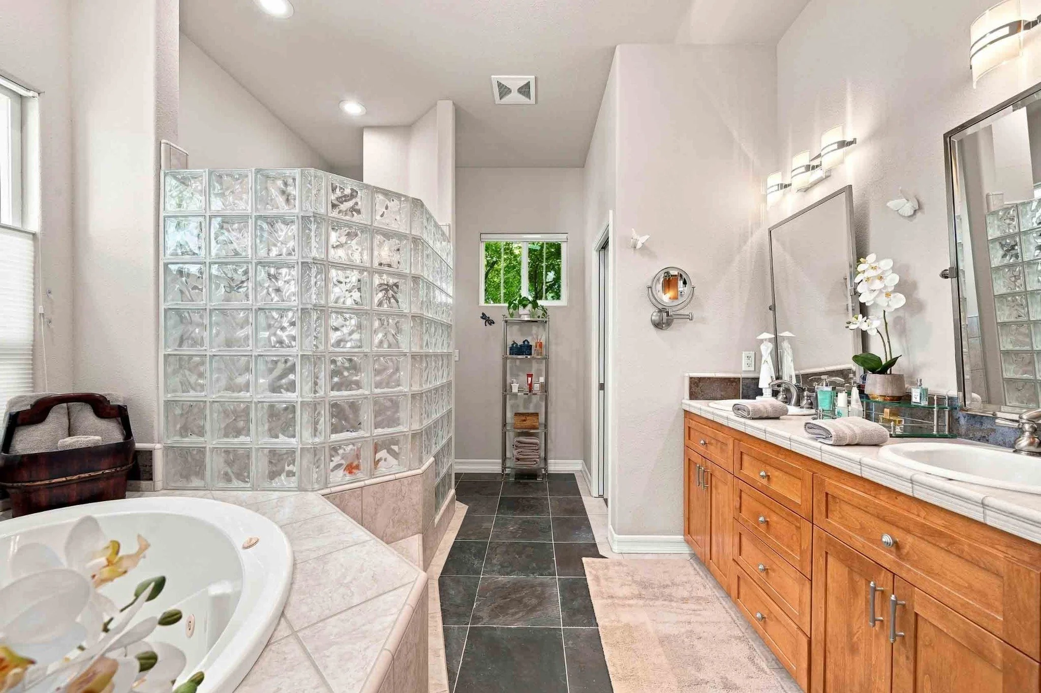 Primary bathroom with a glass-block shower, jetted tub, dual vanity, and slate tile flooring.