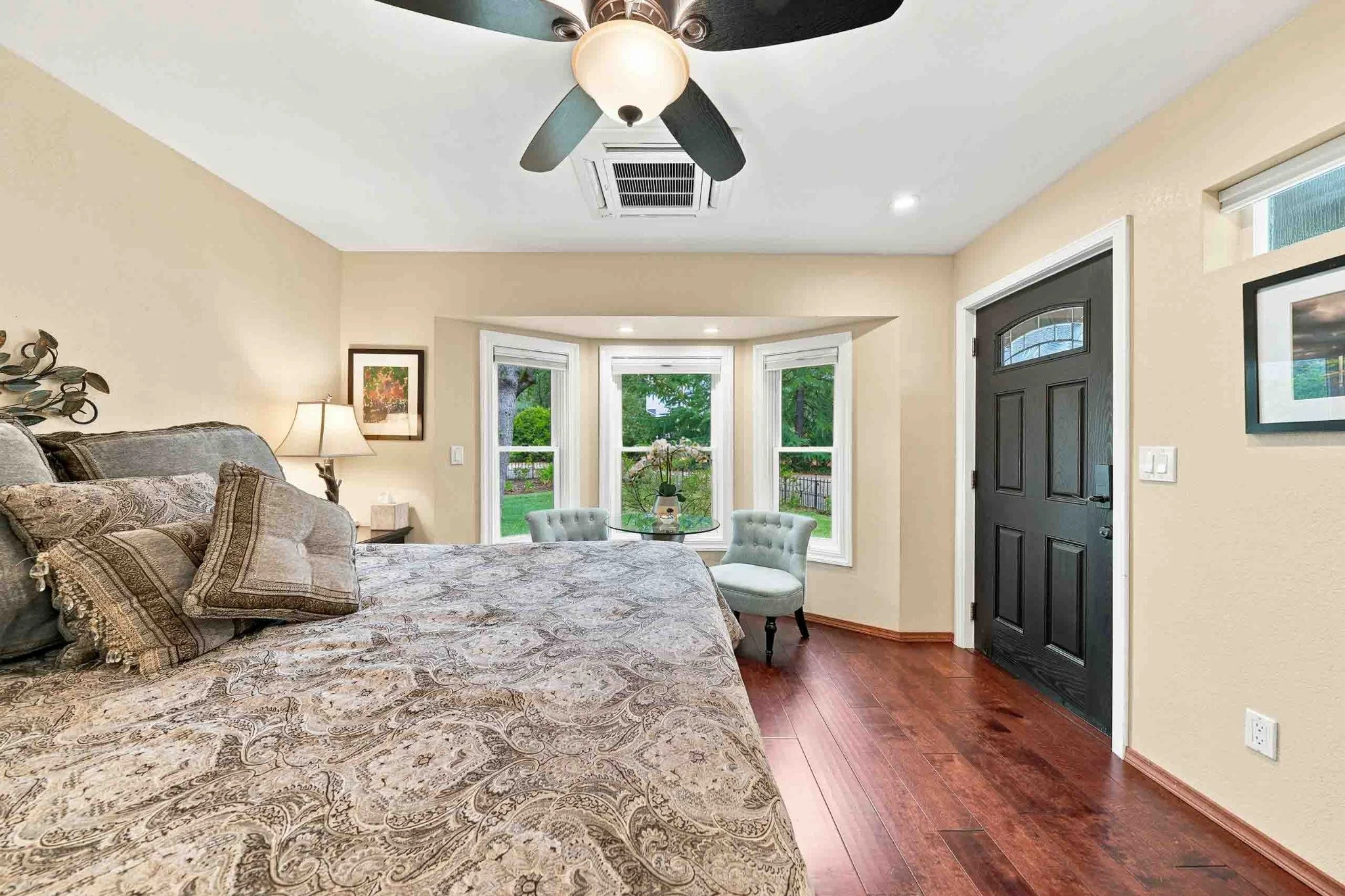 Primary bedroom with hardwood floors, bay windows, a ceiling fan, and a private exterior door.