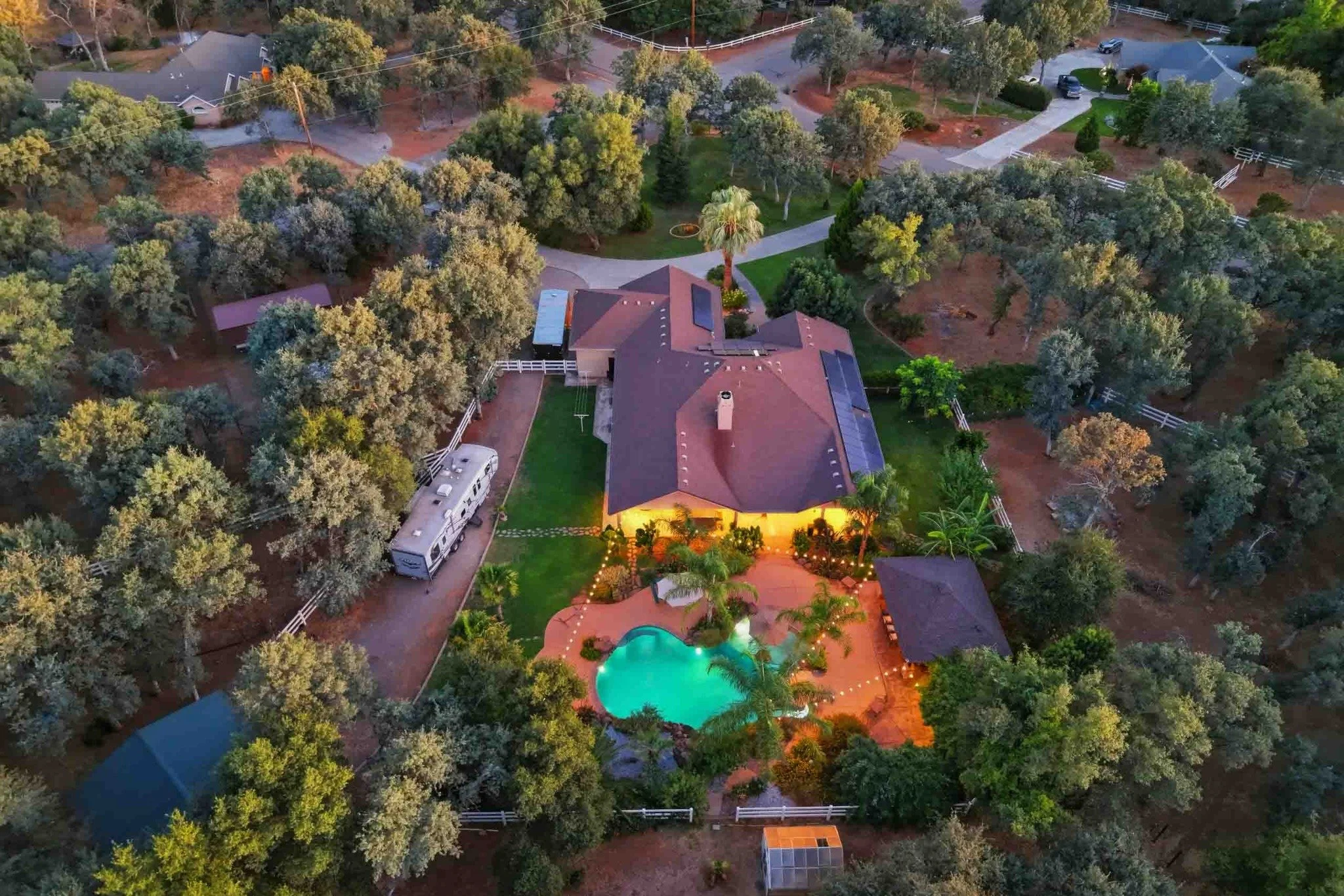 Aerial twilight view of a wooded Redding estate with a pool, landscaping, and outbuildings.