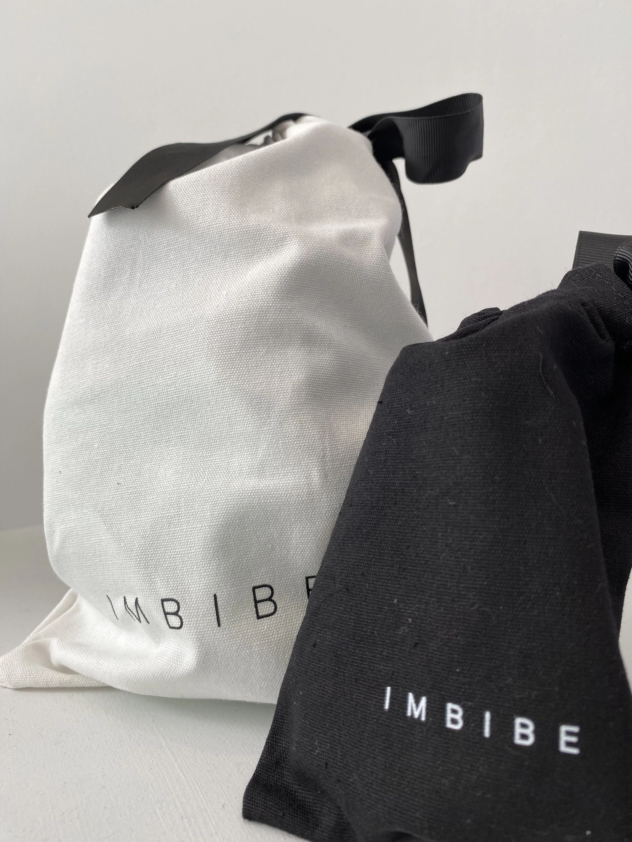 Two cloth bags, one white and one black, with the word 'IMBIBE' printed on them.