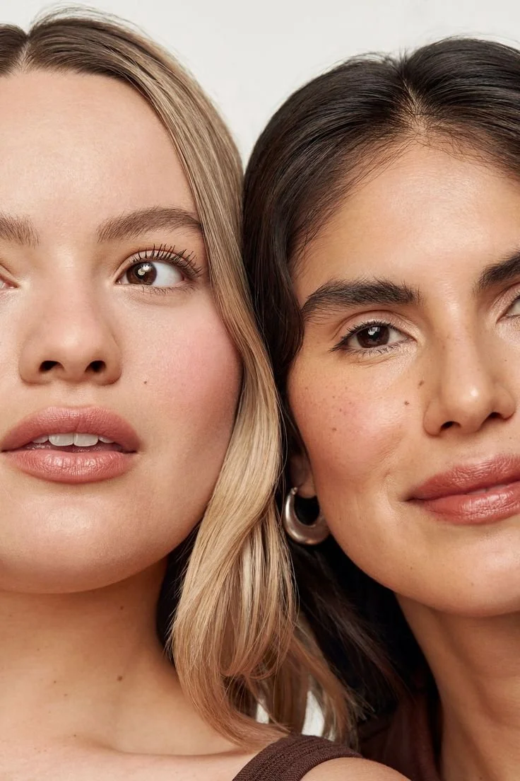 Close-up of two women with diverse skin tones, showcasing natural makeup and different hairstyles, posing side by side.