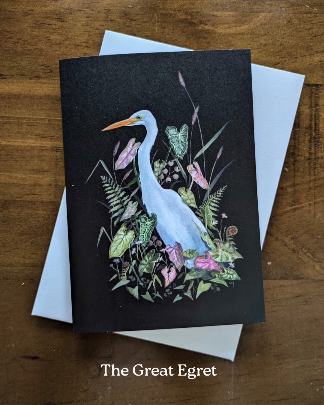 A greeting card with a painted white Great Egret bird surrounded by syngoniums and other plants, on a black background.