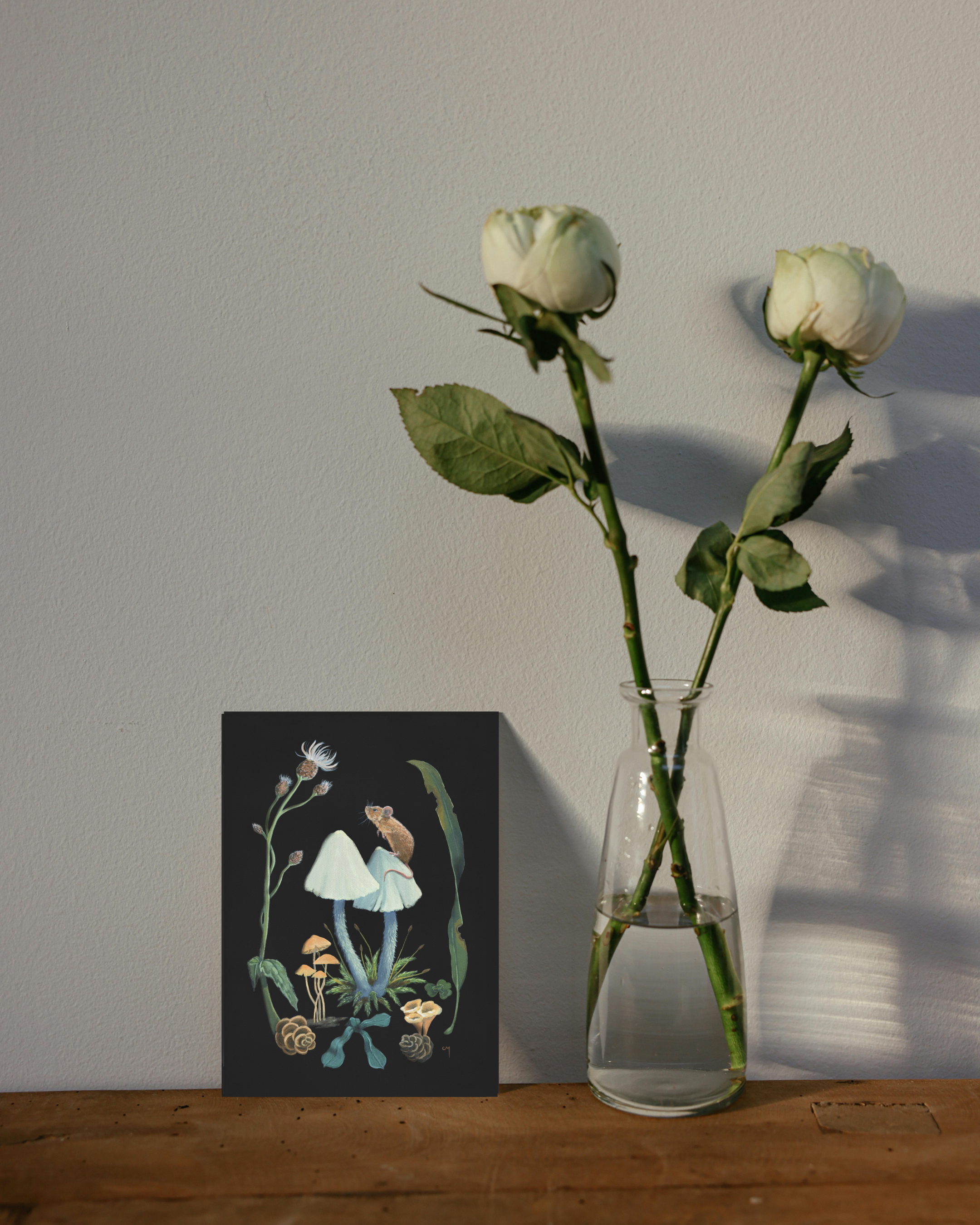 The Field Mouse and Inkcaps wildlife painting greeting card next to flowers.