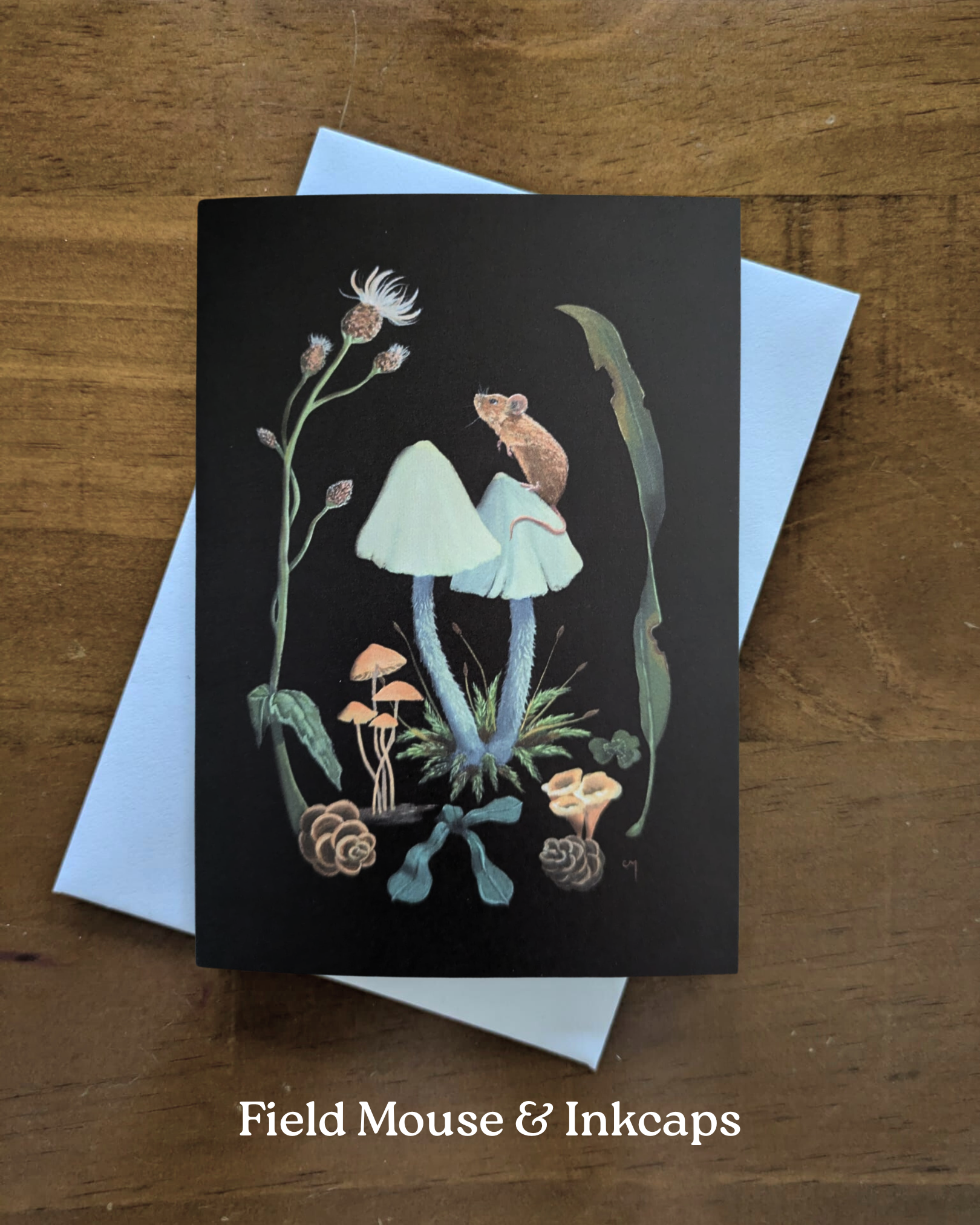 A greeting card with a painted brown mouse on top of a pale blue inkcap mushroom, surrounded by flowers and forest items, on a black background.