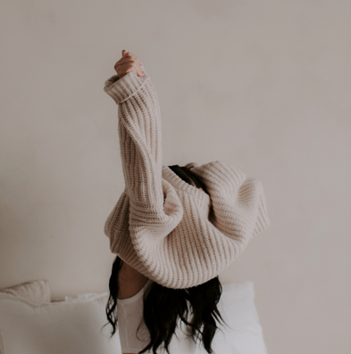 Nahaufnahme einer Frau beim Dehnen und Ausziehen eines Pullovers zur Visualisierung von Körperarbeit, Faszien-Release und Mobilitätstraining im Postpartum-Programm.