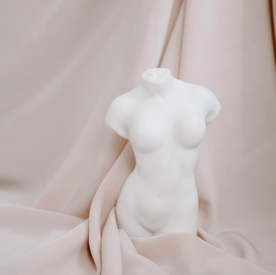 Weiße Skulptur eines weiblichen Torsos vor sanftem Hintergrund – Symbol für die anatomische Ästhetik und die körperliche Integrität der Frau nach der Geburt.