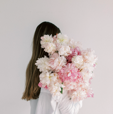 Ästhetische Nahaufnahme einer Frau mit rosa Pfingstrosen als Symbol für die ganzheitliche Begleitung und die hormonelle Regeneration im Postpartum-Training.