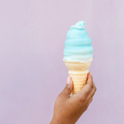 Eine Hand hält ein hellblaues Softeis vor lila Hintergrund – Symbol für Leichtigkeit, Belohnung und die Freude am Business-Aufbau als selbstständige Therapeutin.