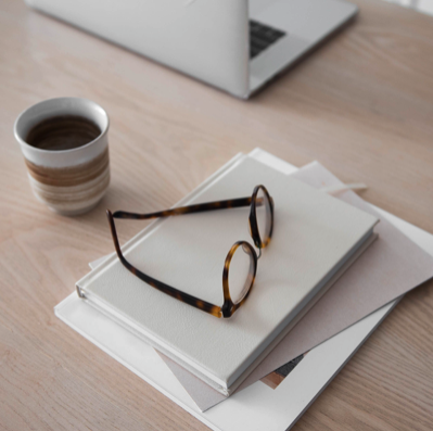 Hell gestalteter Arbeitsplatz mit Notizbuch und Brille zur Illustration der fachlichen Spezialisierung und anatomischen Grundlagen in der Postpartum Pro Ausbildung.