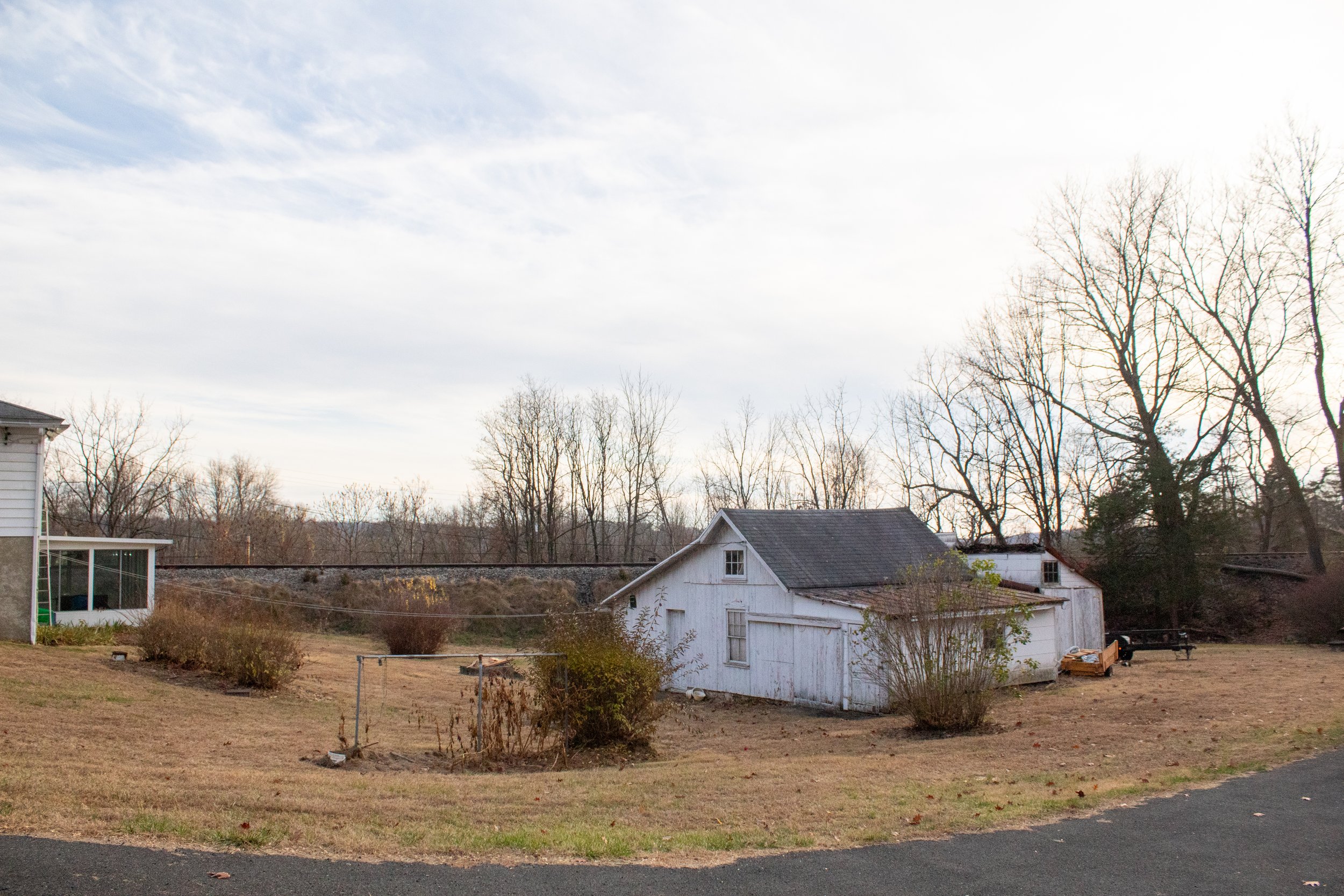 Rural scene with a white wooden shed, barren trees, and dry grass