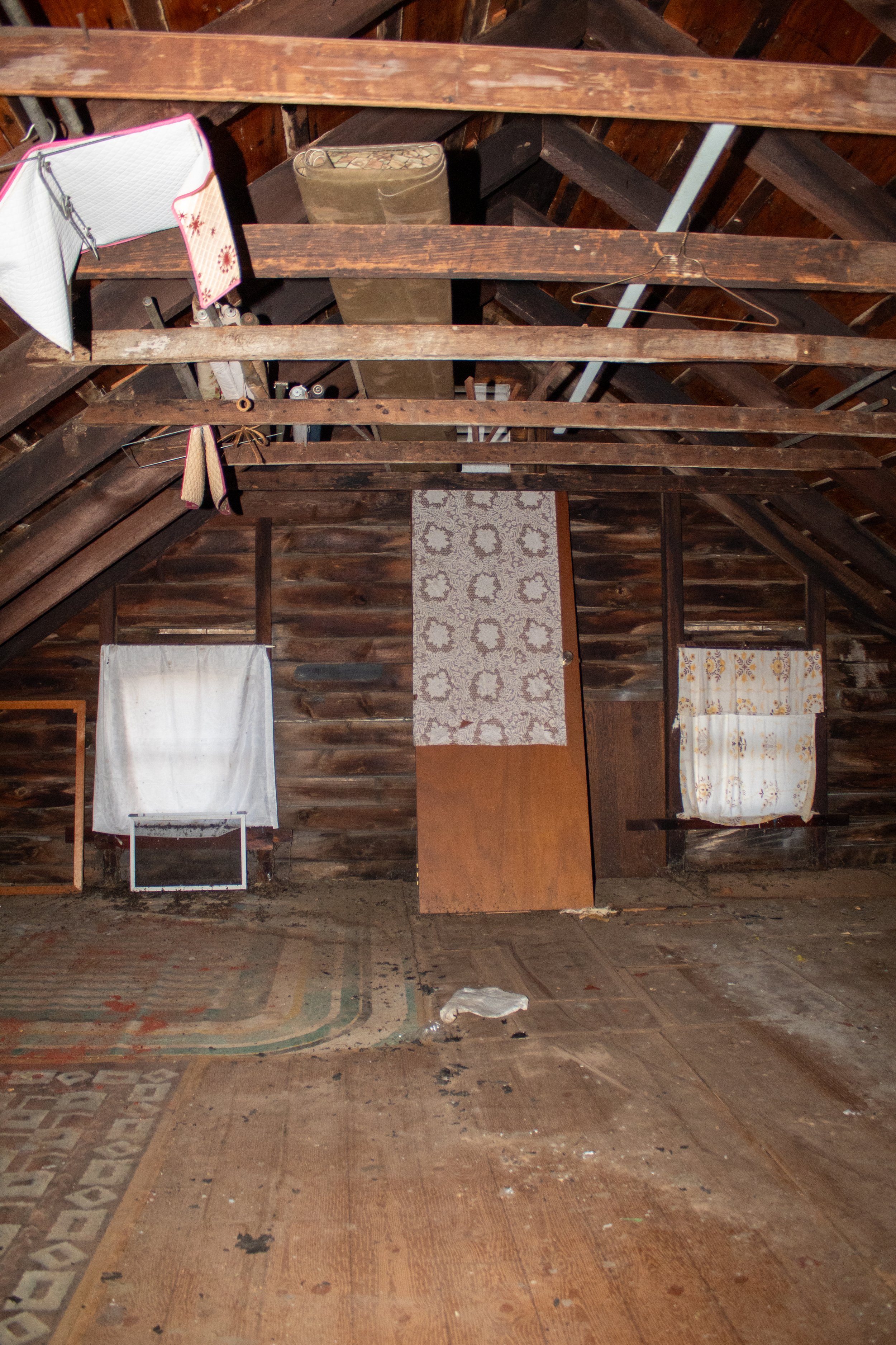 Old attic with wooden beams, curtains, and scattered items