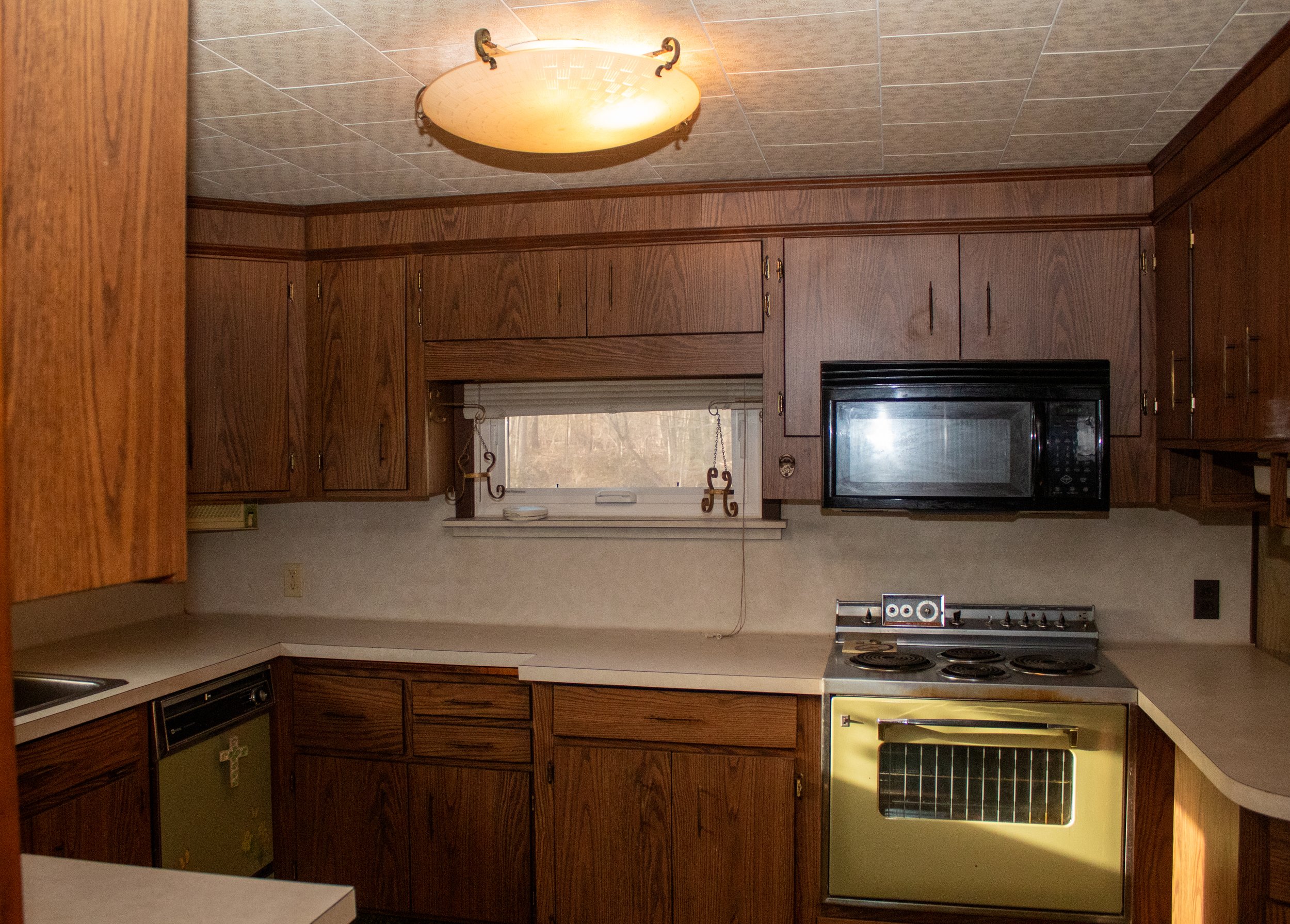 Vintage kitchen with wood cabinets, an old green oven, black microwave, and beige countertops.