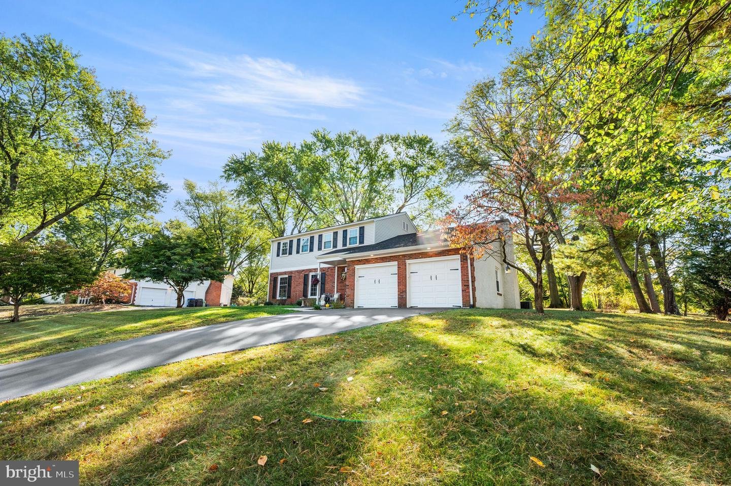 Suburban house with two-car garage and driveway surrounded by trees in a green lawn setting.